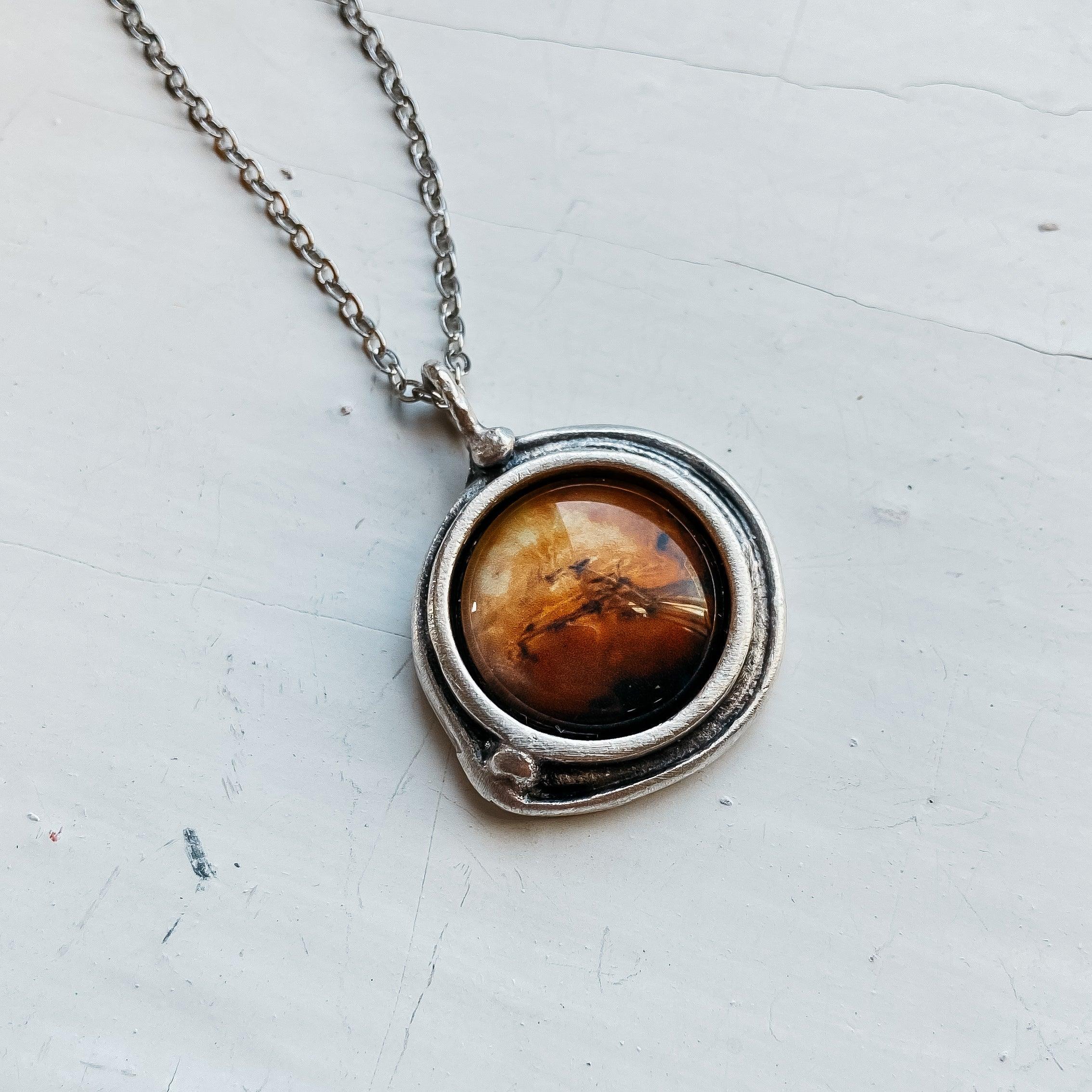 Silver pendant necklace with round amber stone on white textured surface