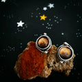 Artist-designed cosmic stud earrings with galaxy motifs, displayed on a textured stone, starry background