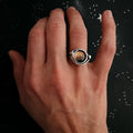 Hand wearing a silver ring with a round, amber-colored stone on a starry black background