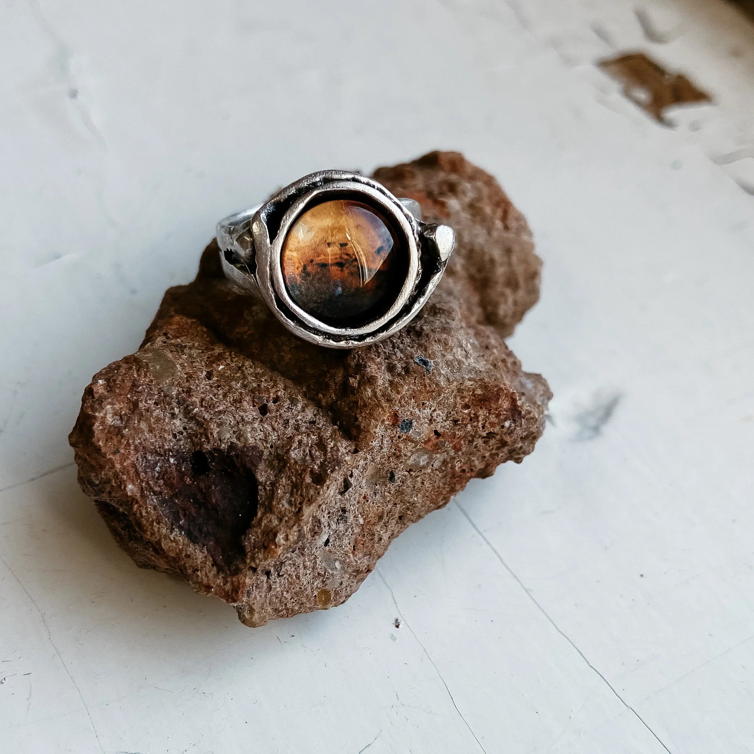 Silver ring with round amber stone on rough brown rock on white surface