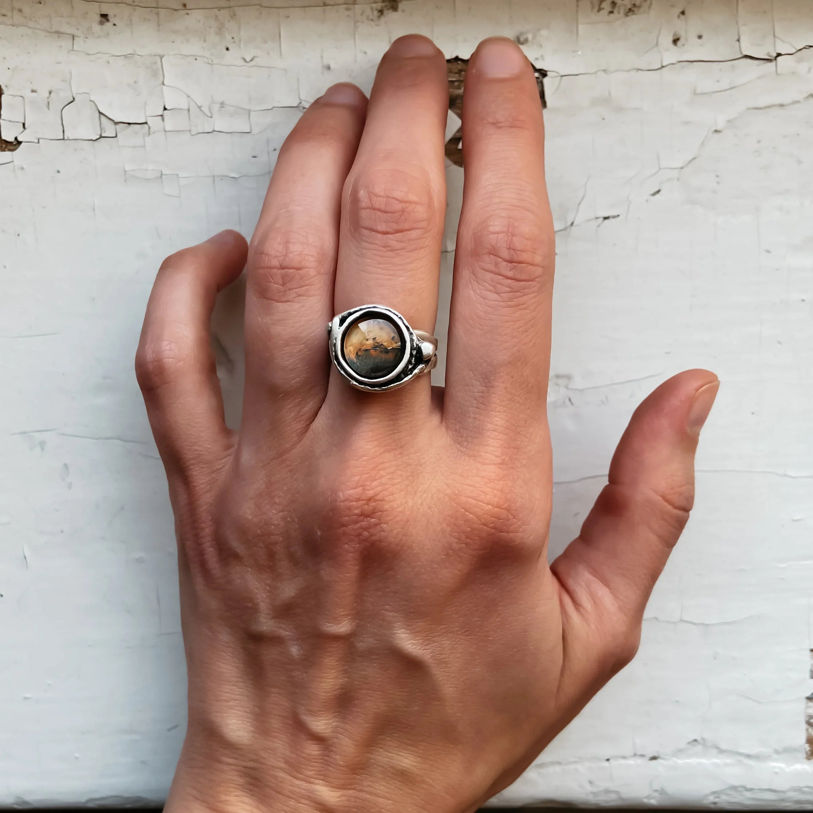 Hand wearing a silver ring with a round, amber-colored stone against a cracked white wooden background