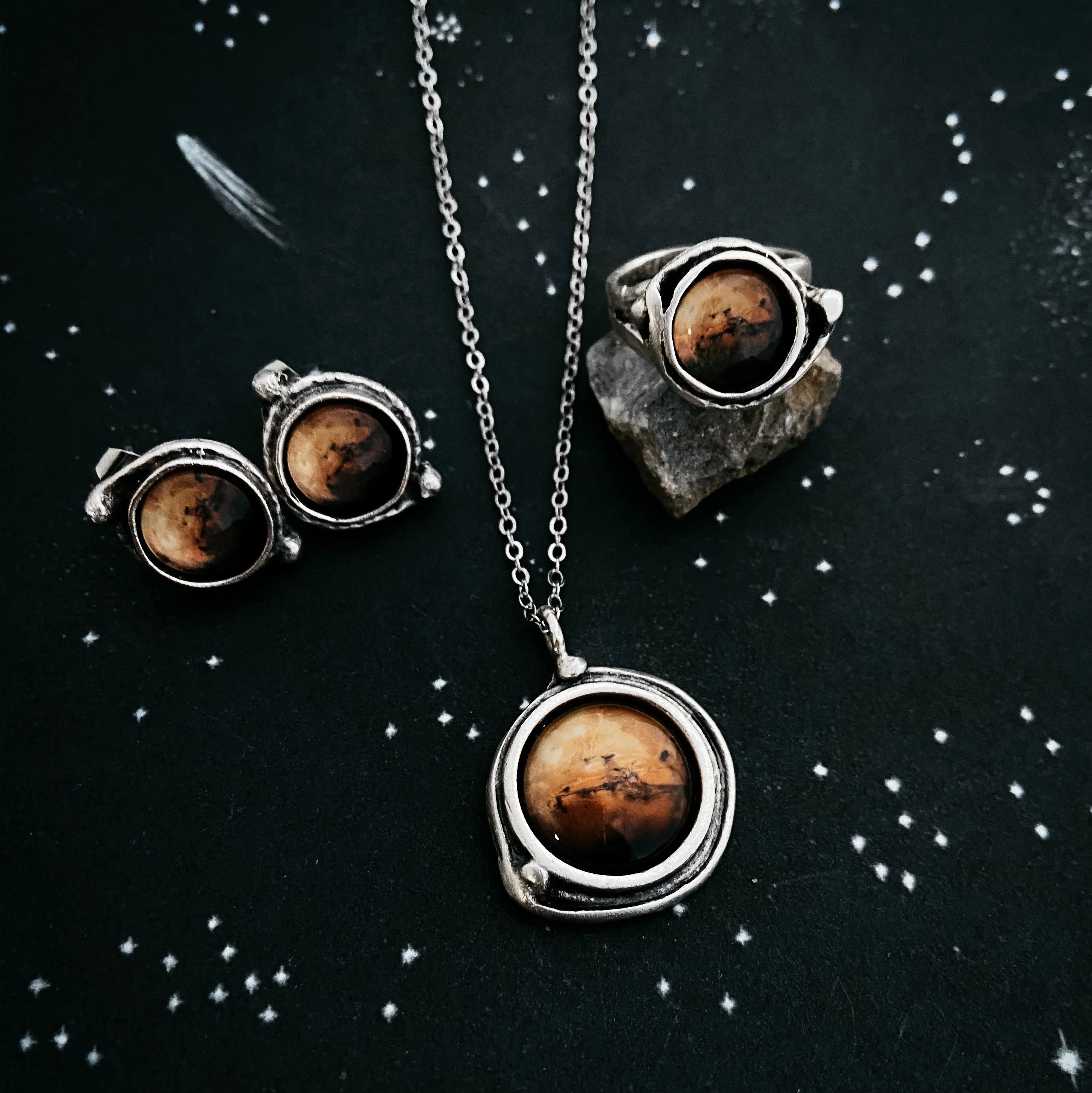 Artist-designed cosmic jewelry set with pendant, earrings, and ring on starry background