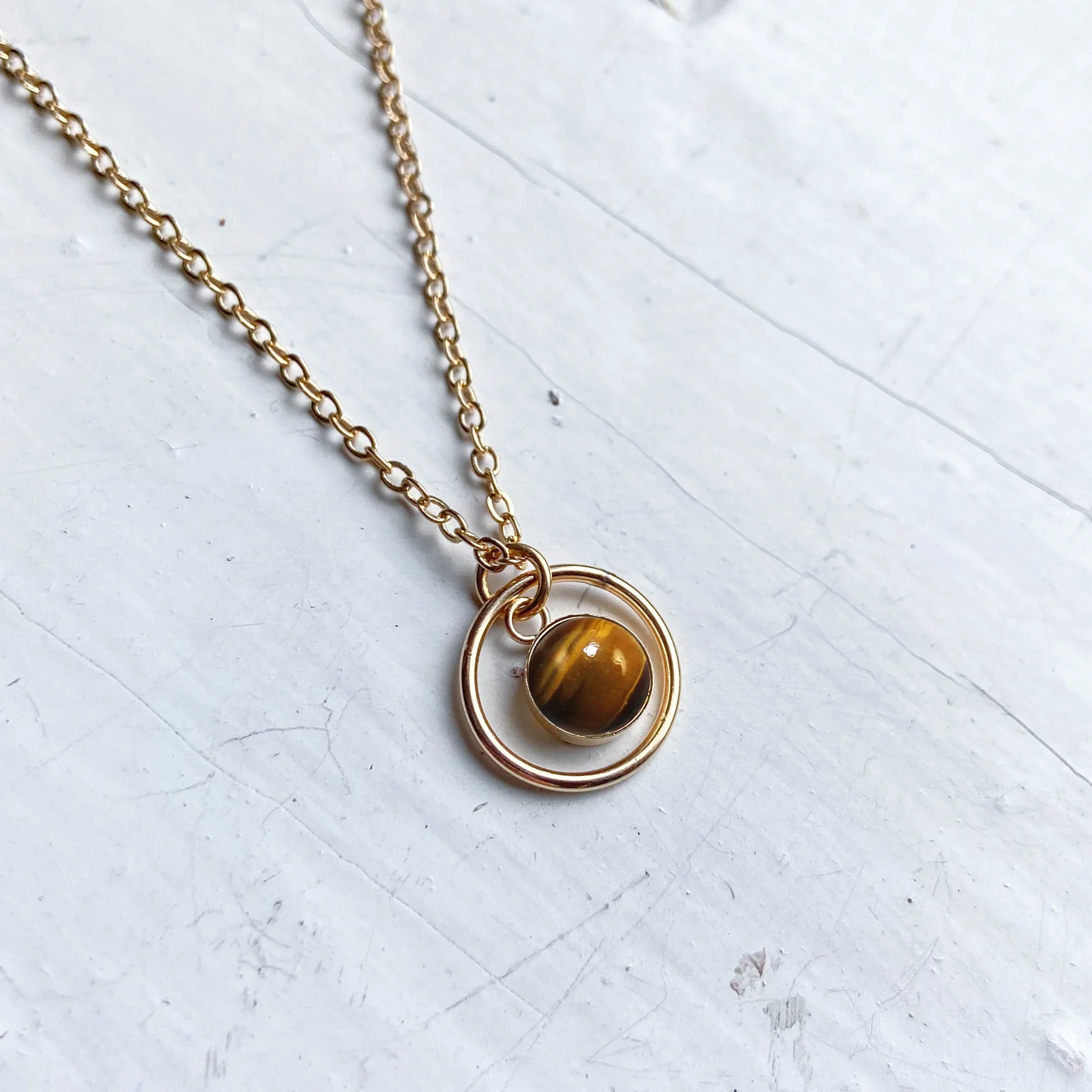 Gold chain necklace with circular pendant and tiger’s eye gemstone on white background