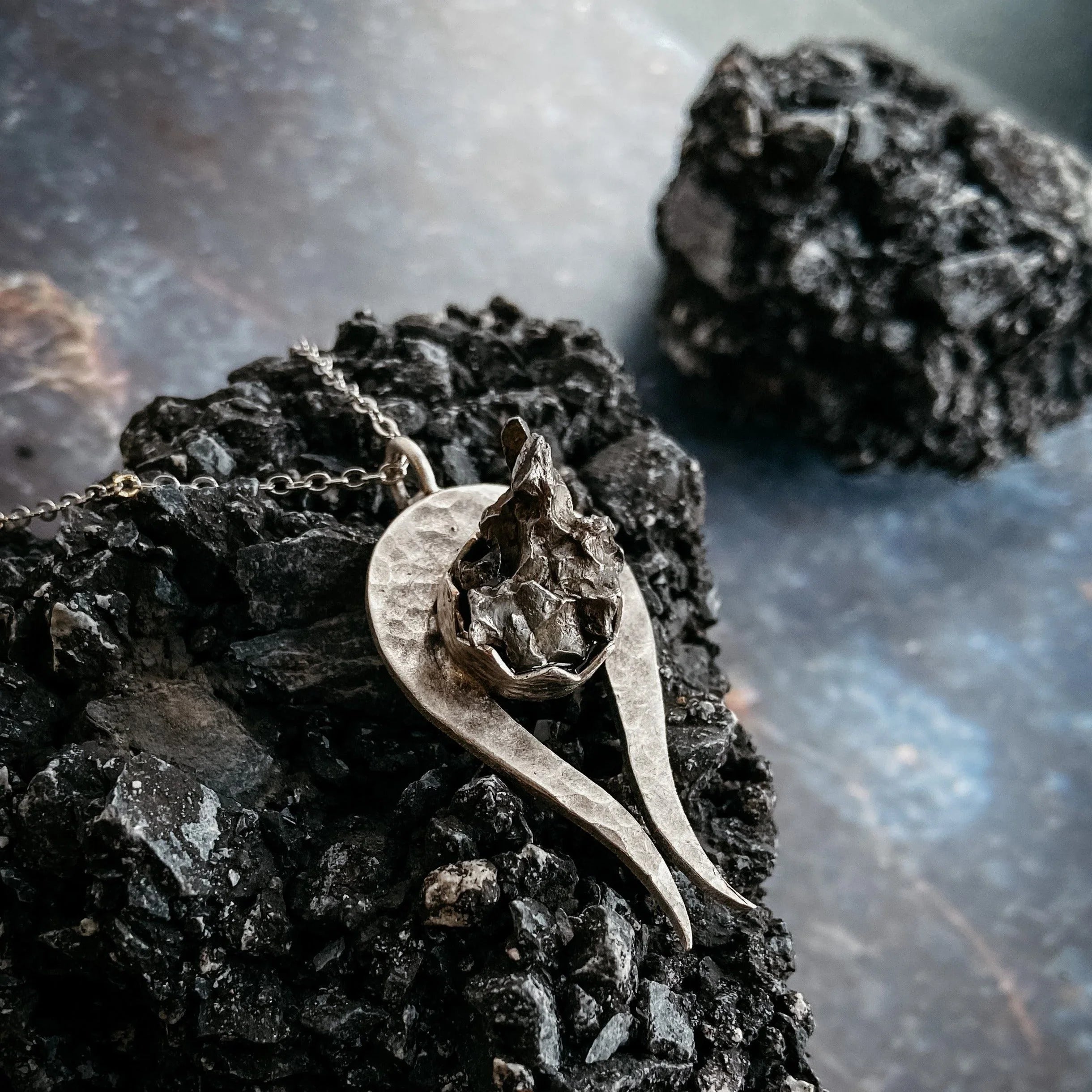 Handcrafted silver pendant with rough textured centerpiece on black volcanic rock background