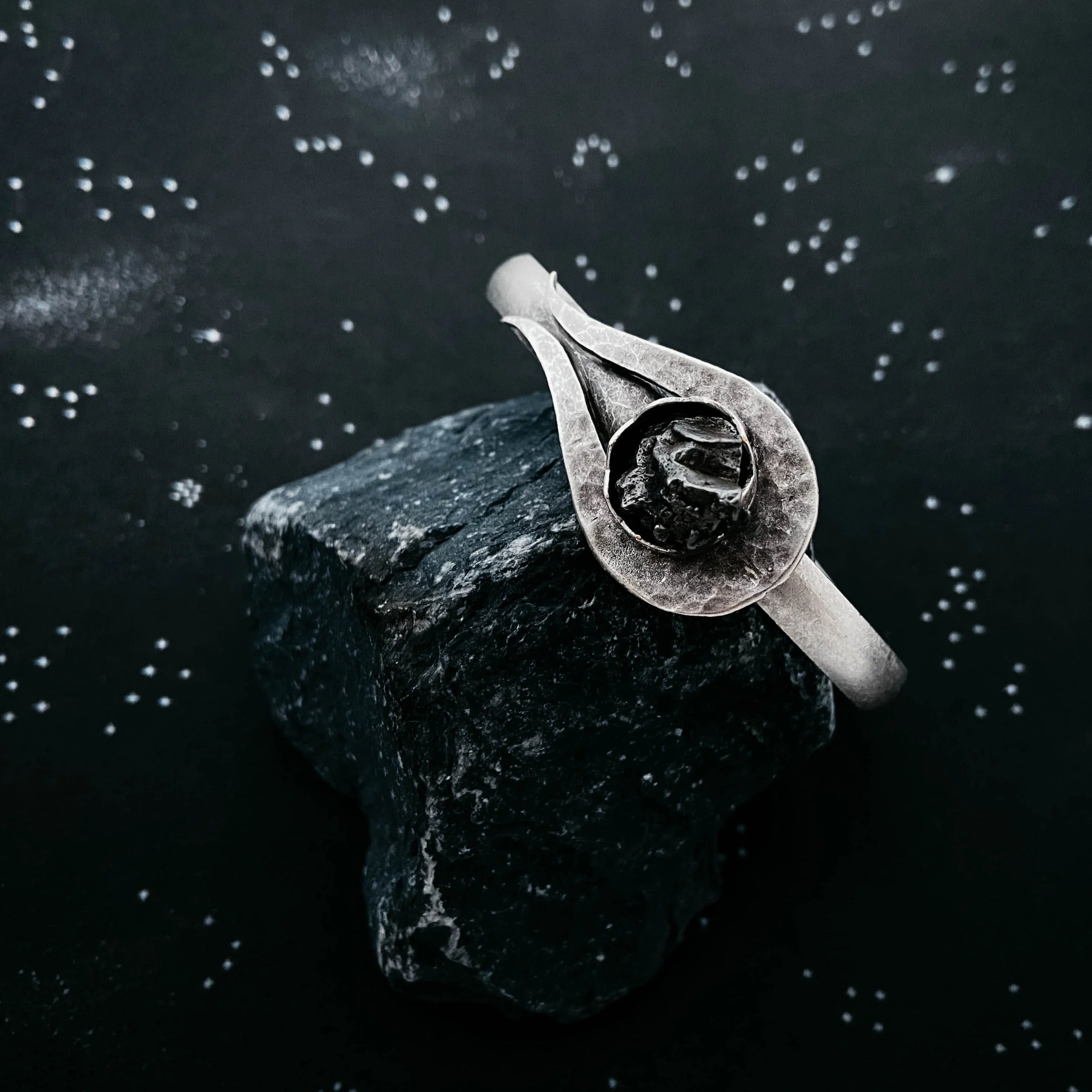 Handcrafted silver ring with textured black stone on dark rock background