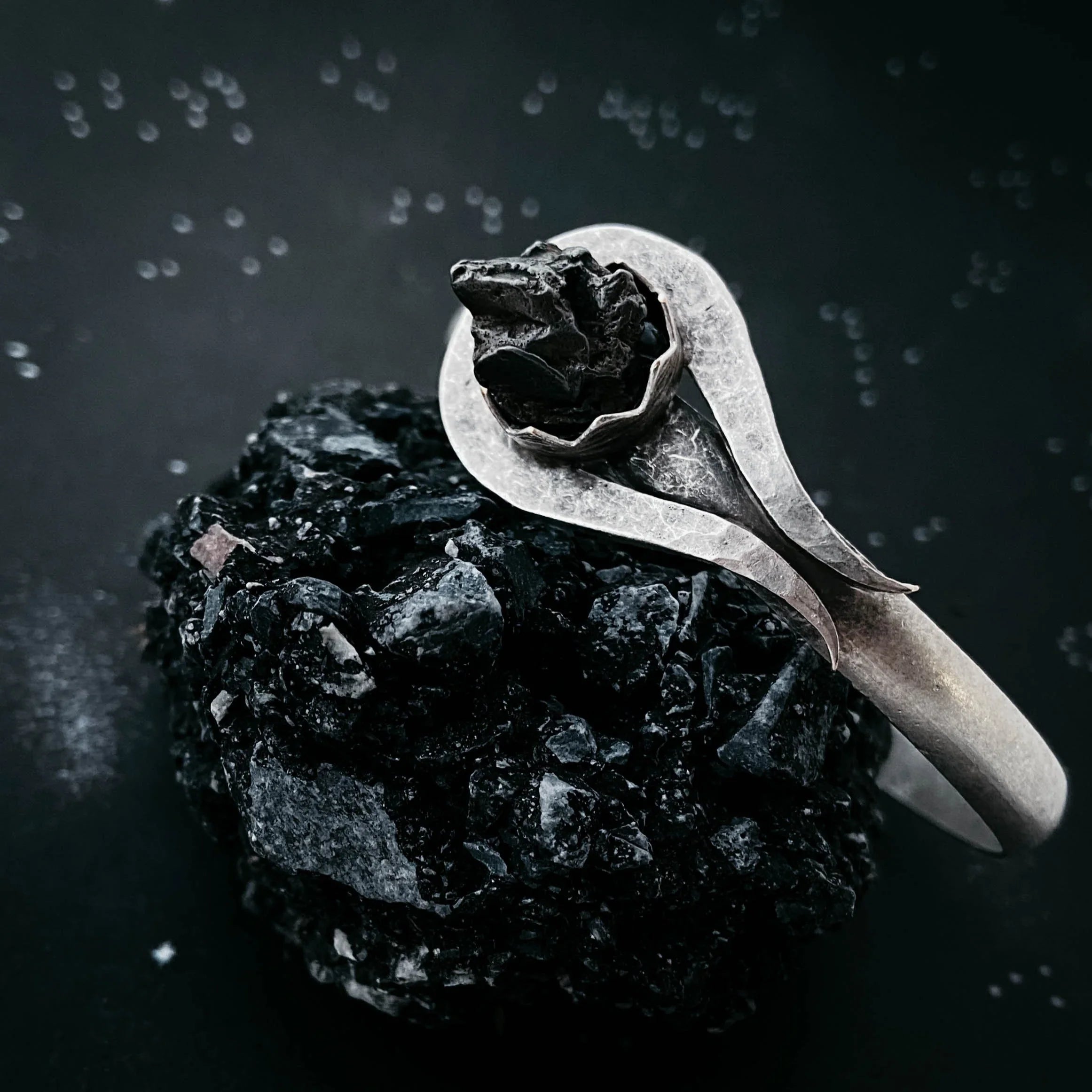 Silver ring with a rough black raw stone setting on a dark textured rock background