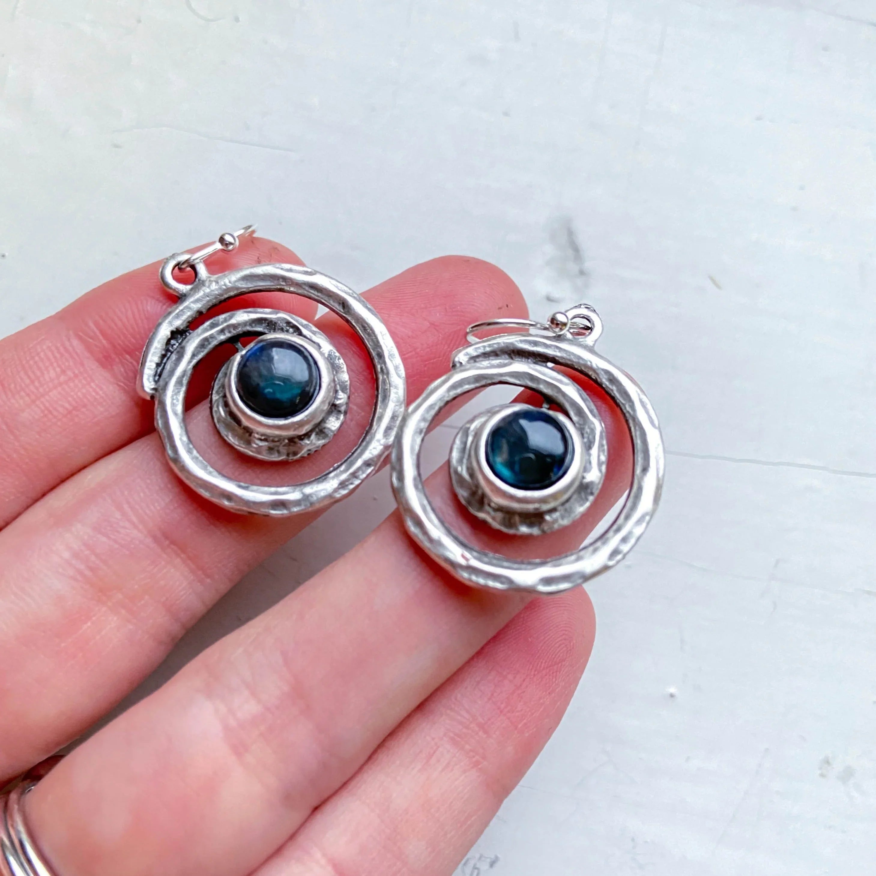 Hand holding artisan silver spiral earrings with dark blue gemstone centers, Qu!rk Boutique