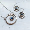 Handcrafted silver spiral necklace and earrings set with blue stones on white background