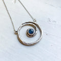 Handmade silver spiral necklace with blue stone pendant on light background, cosmic jewelry