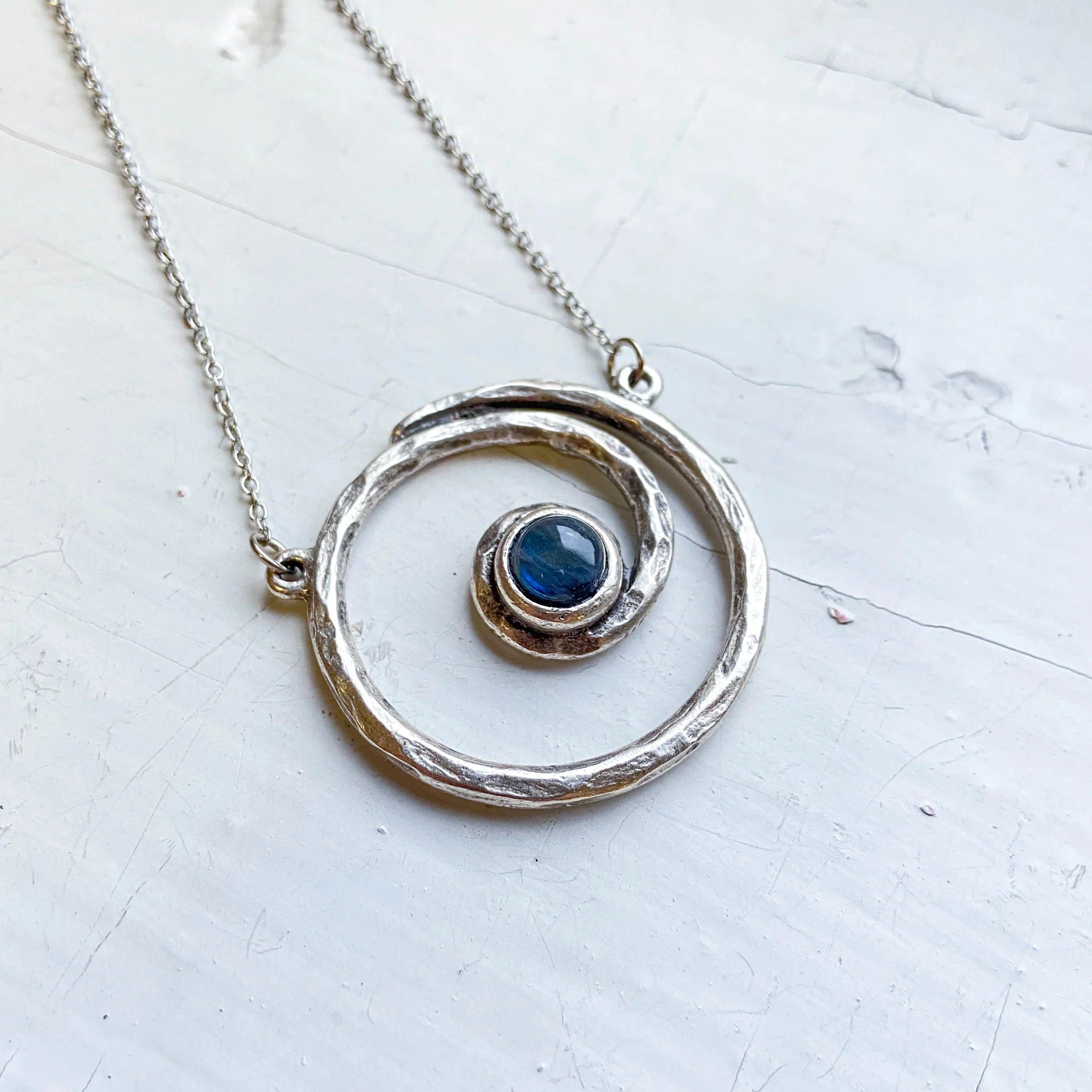 Handmade silver spiral necklace with blue stone pendant on light background, cosmic jewelry