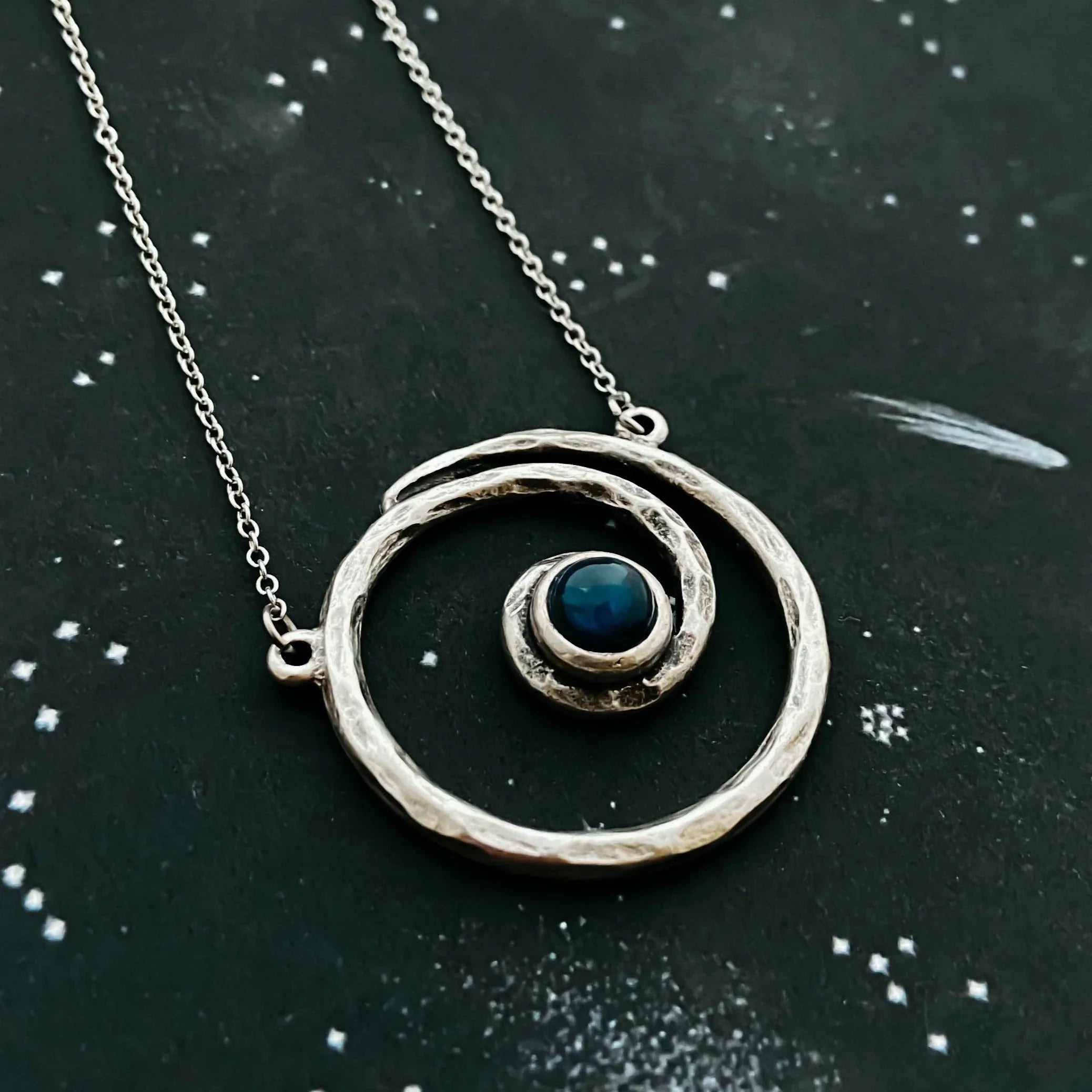 Silver spiral necklace with a blue stone on a cosmic starry background, Qu!rk Boutique