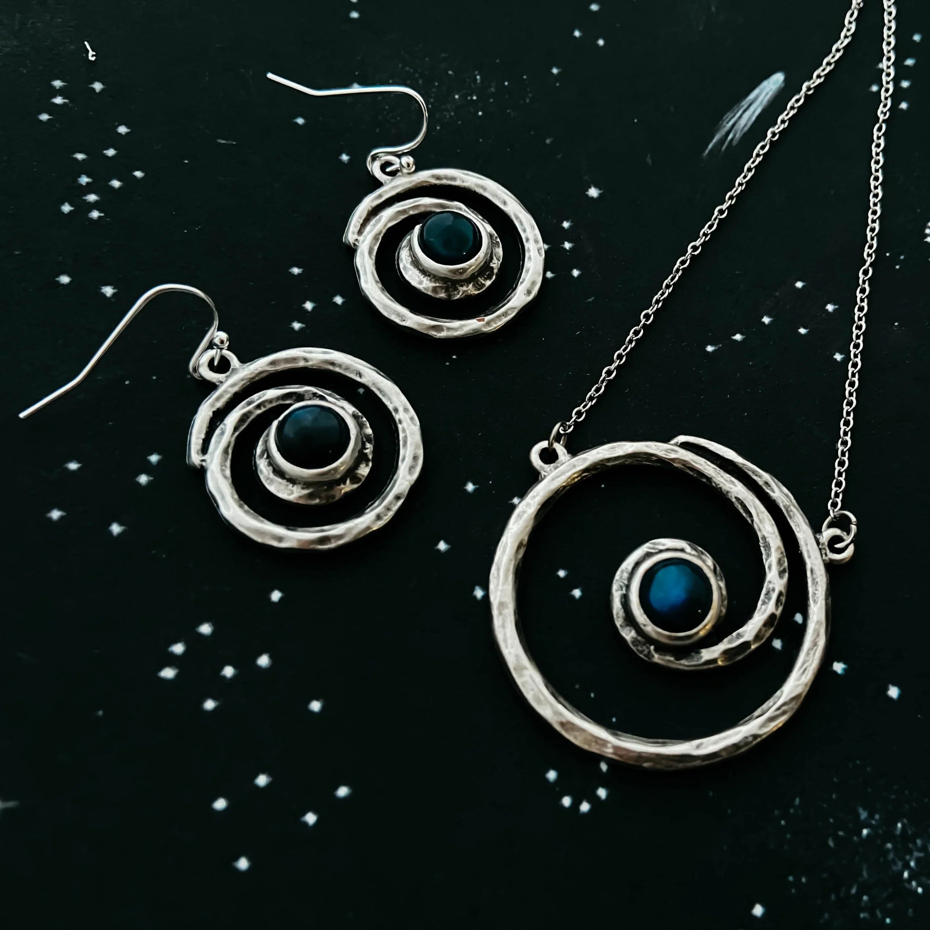 Cosmic spiral silver jewelry set with blue stones on a star-patterned background at Qu!rk Boutique