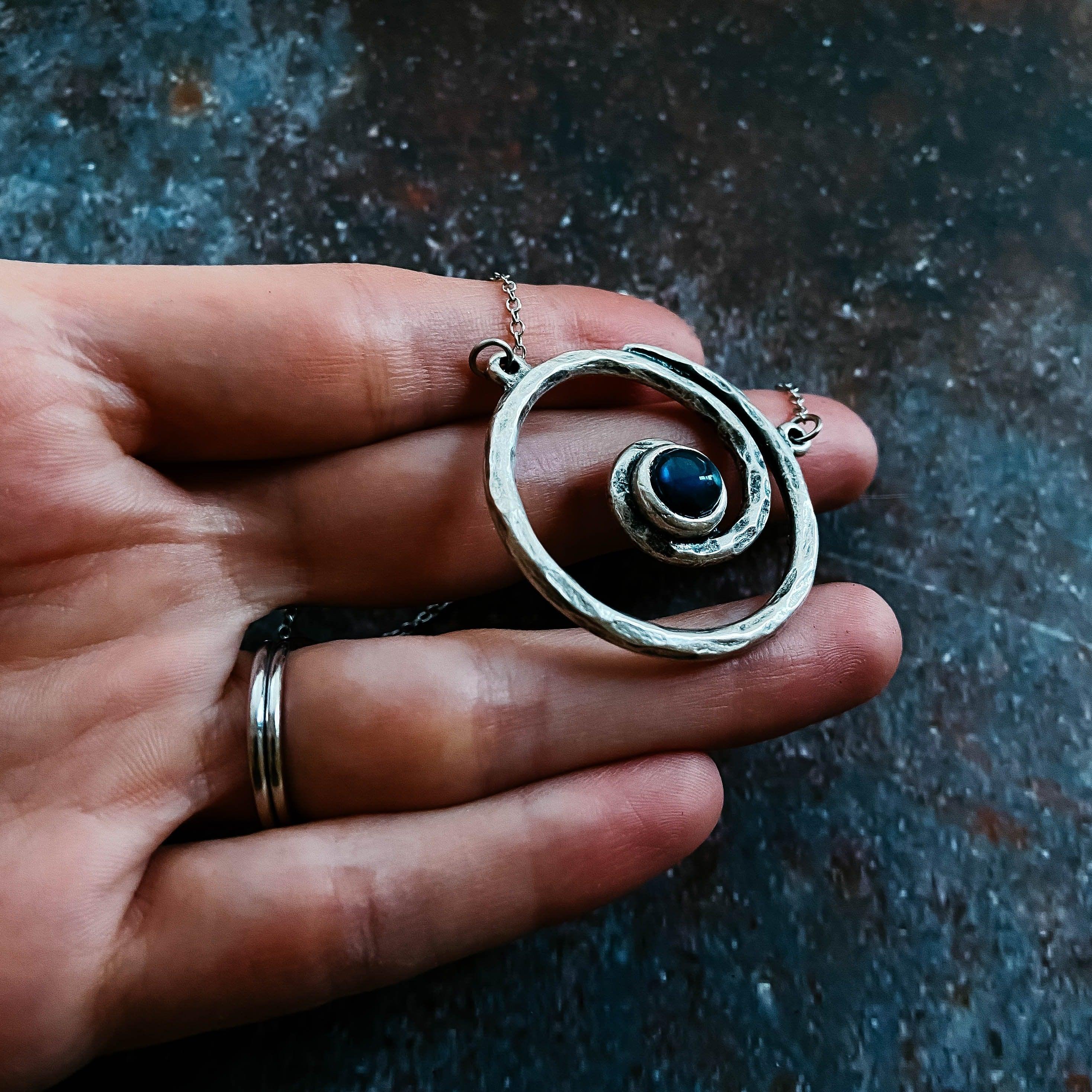 Hand holding cosmic-inspired silver pendant with blue stone from Qu!rk Boutique