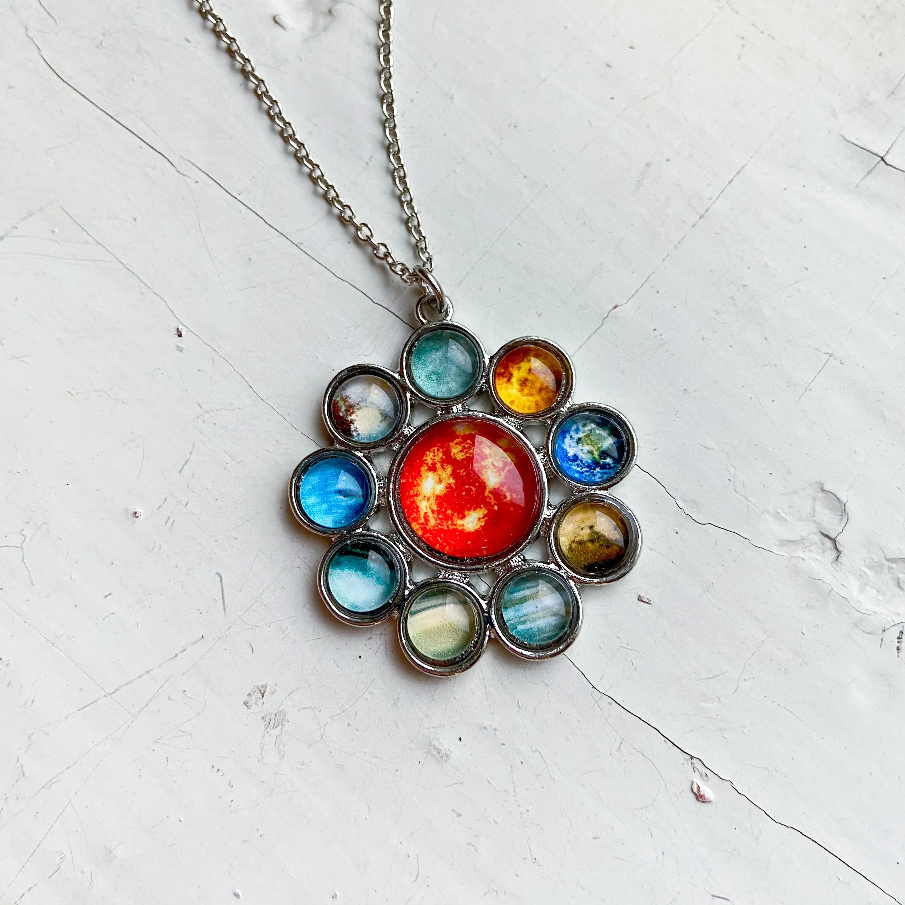 Silver necklace pendant featuring colorful glass planets in solar system design on white textured surface