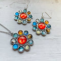 Silver solar system necklace and earrings with colorful planet designs on white surface