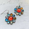 Silver earrings with multicolored planet designs arranged in a circular pattern on a cracked white surface