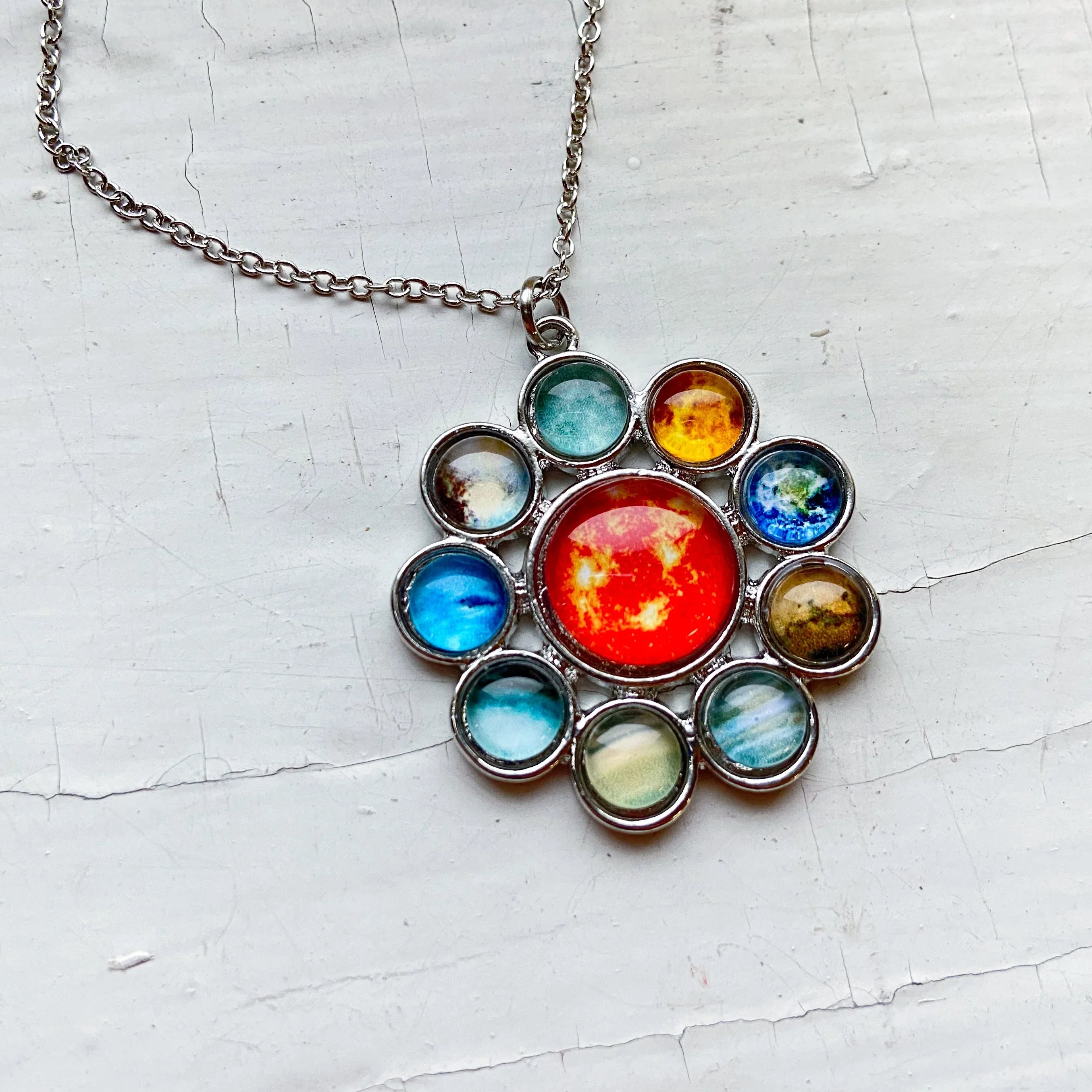 Silver necklace pendant featuring a solar system design with colorful planet glass cabochons on white surface
