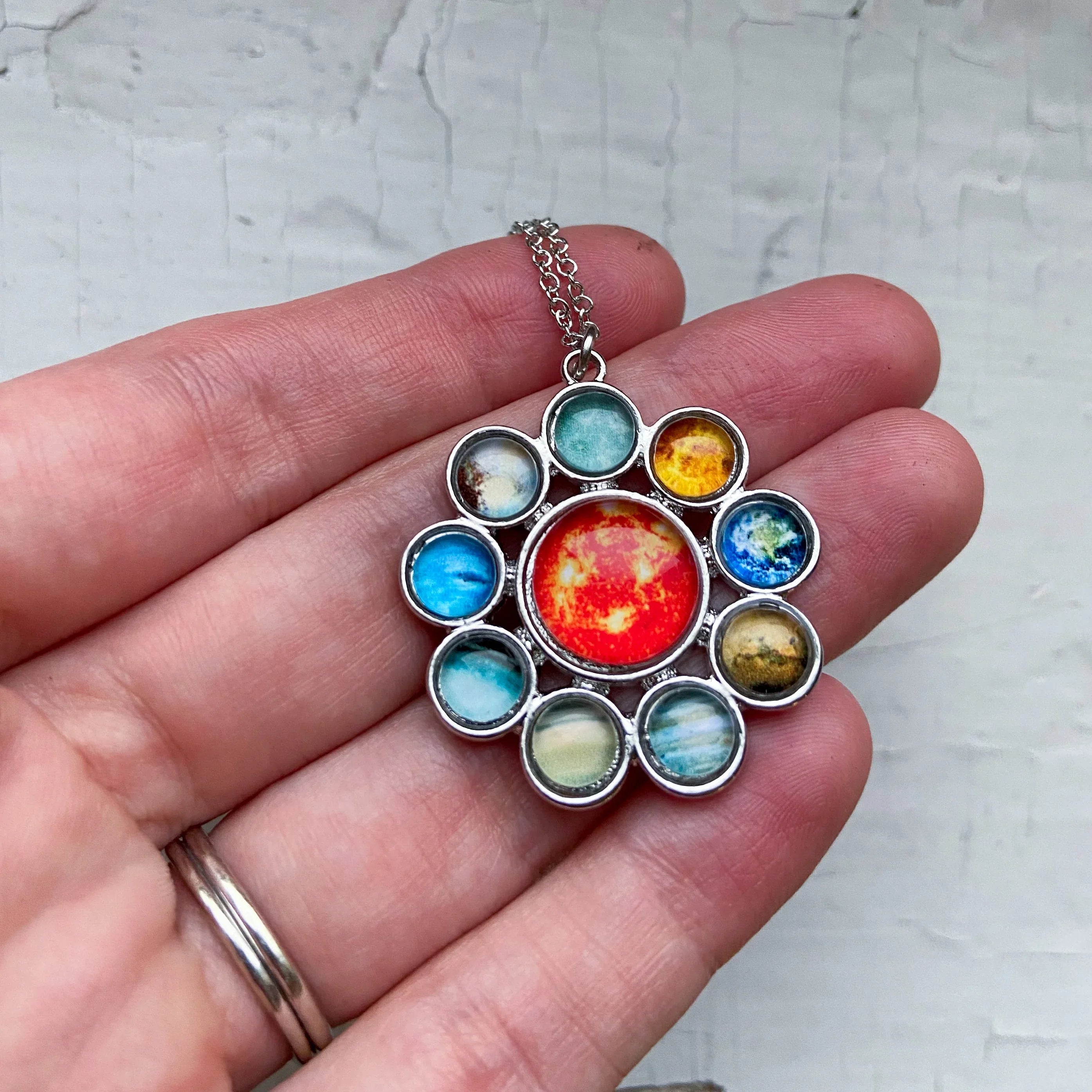 Hand holding a solar system pendant necklace with colorful planet and sun charms