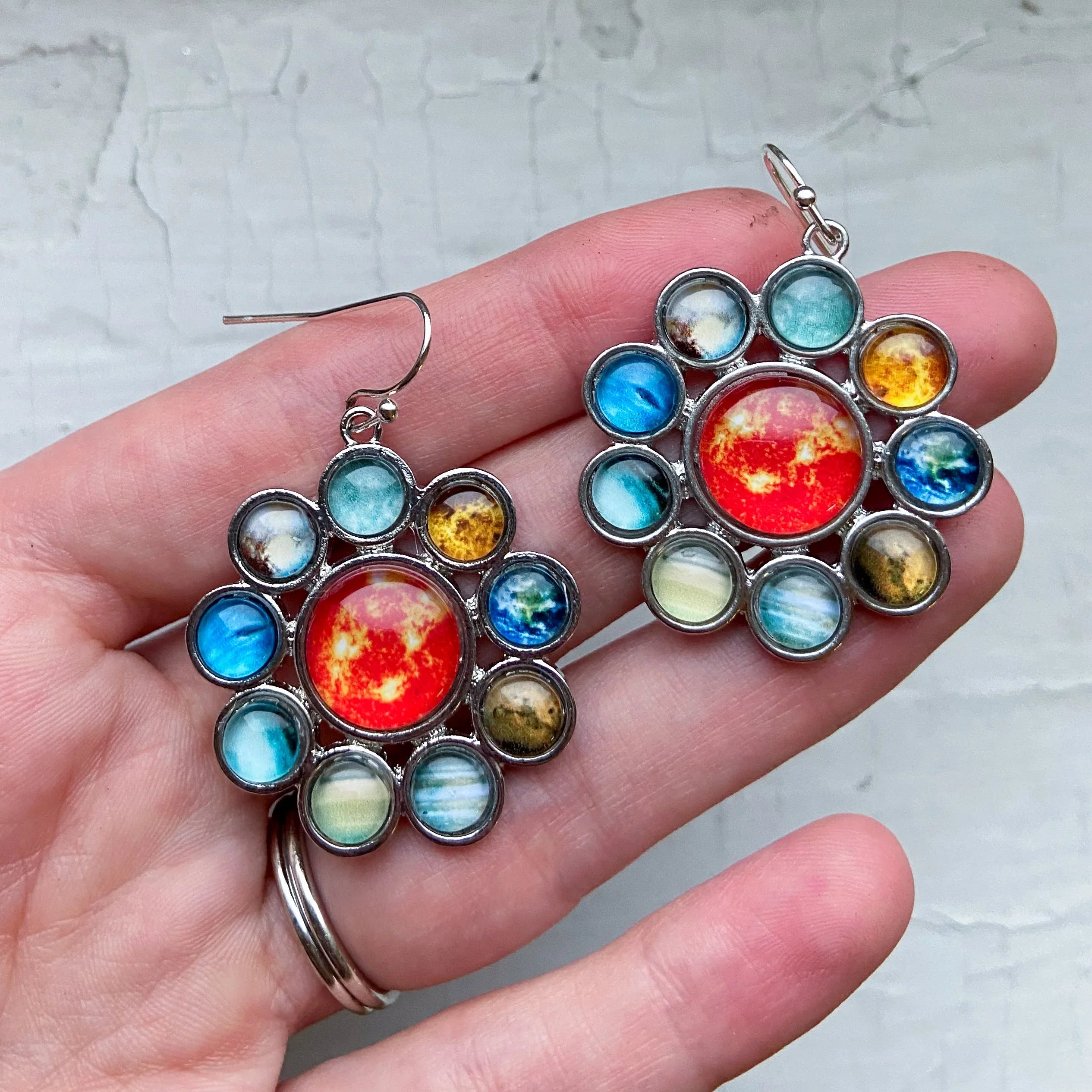Hand holding silver-tone solar system planet earrings with colorful planet designs