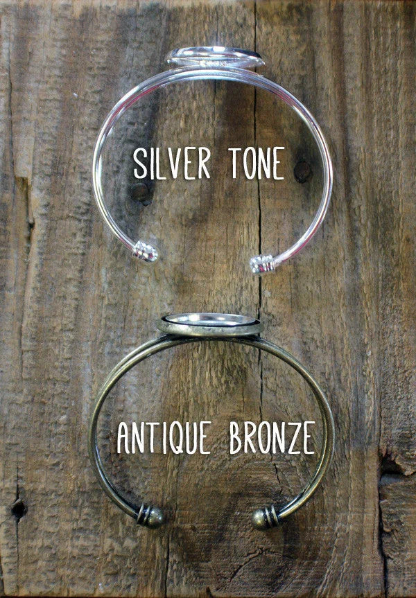 Silver tone and antique bronze open cuff bracelets displayed on rustic wooden background