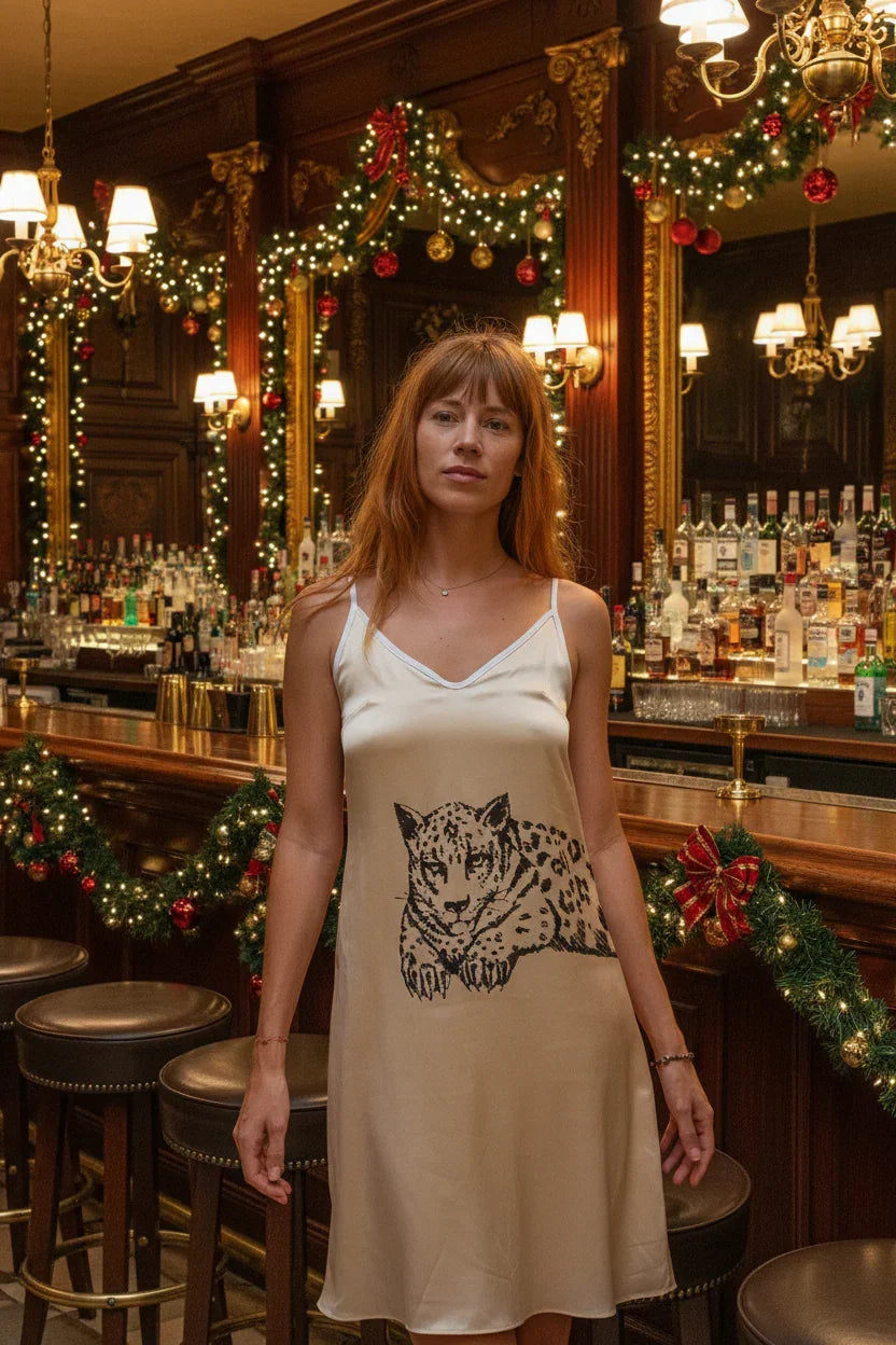 Woman in beige dress with leopard print standing in festive bar decorated with garlands and lights