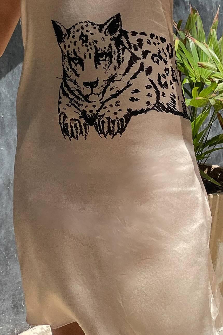 Beige satin dress with black leopard graphic print worn indoors near green plant