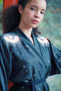 Young woman with curly hair wearing a black kimono robe with eye and starry pattern indoors