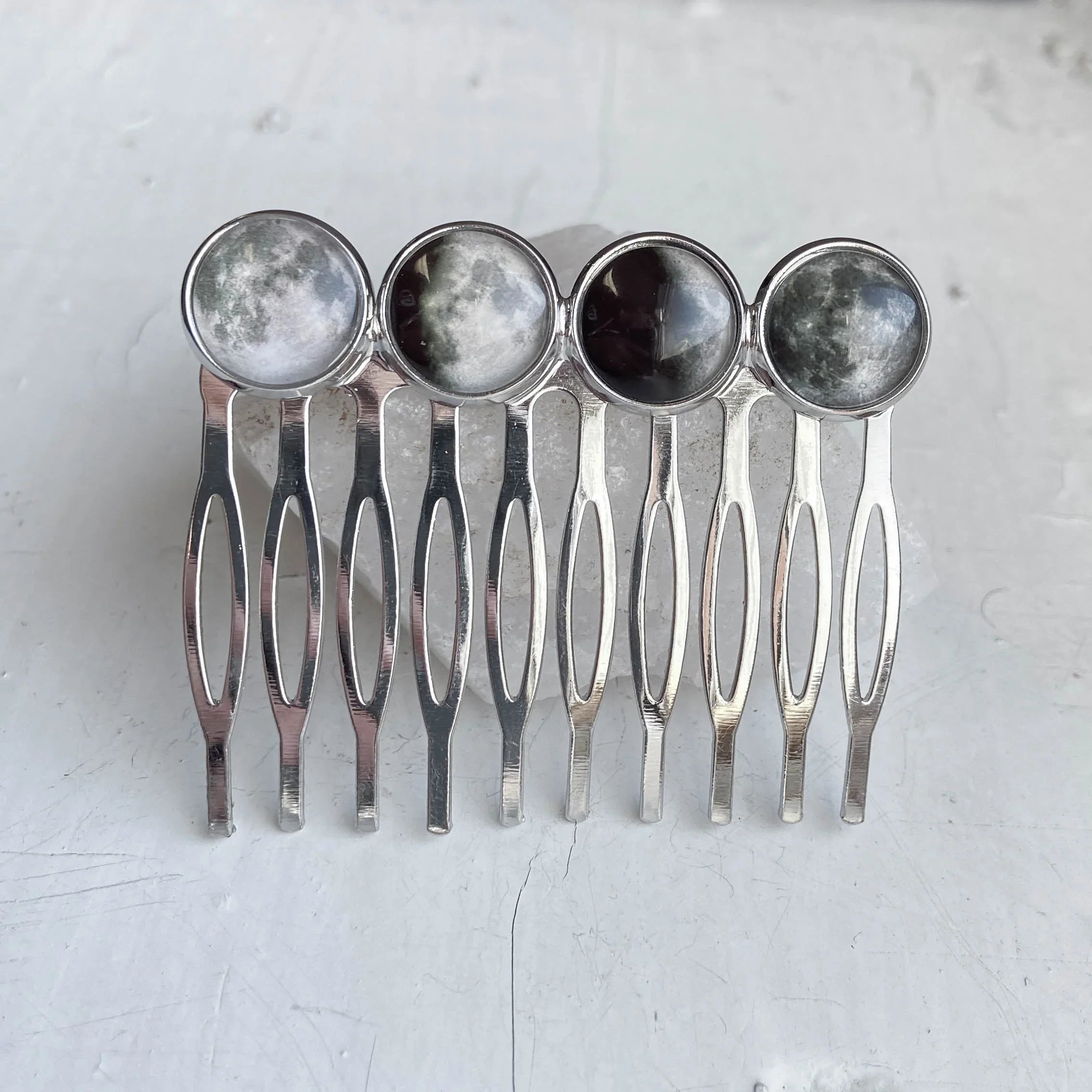Silver metal hair combs with round moon phase designs on top arranged in a row on a light surface