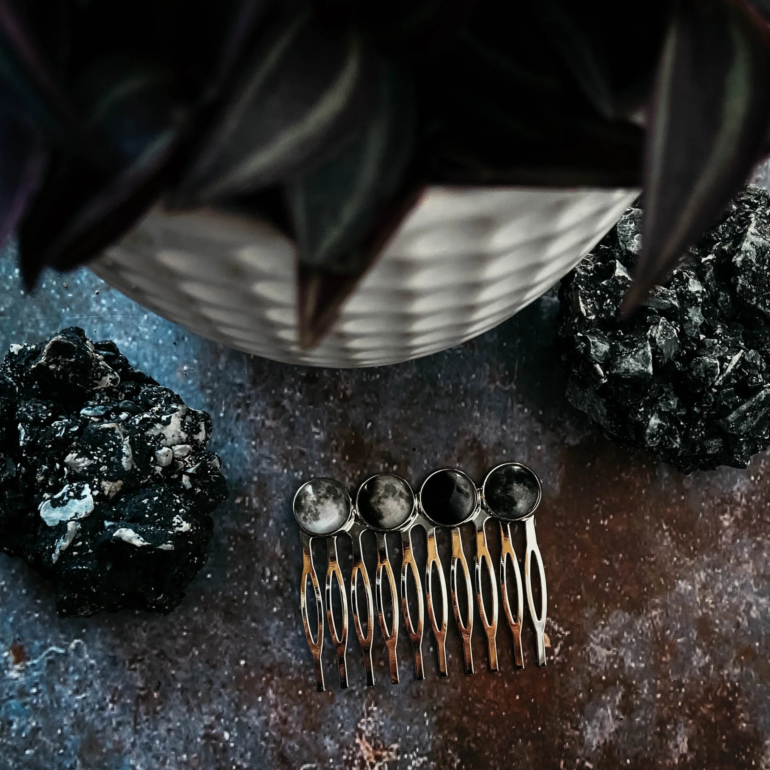 Silver hair clip with moon phase charms on rustic blue and brown surface with black rocks and blurred plant pot