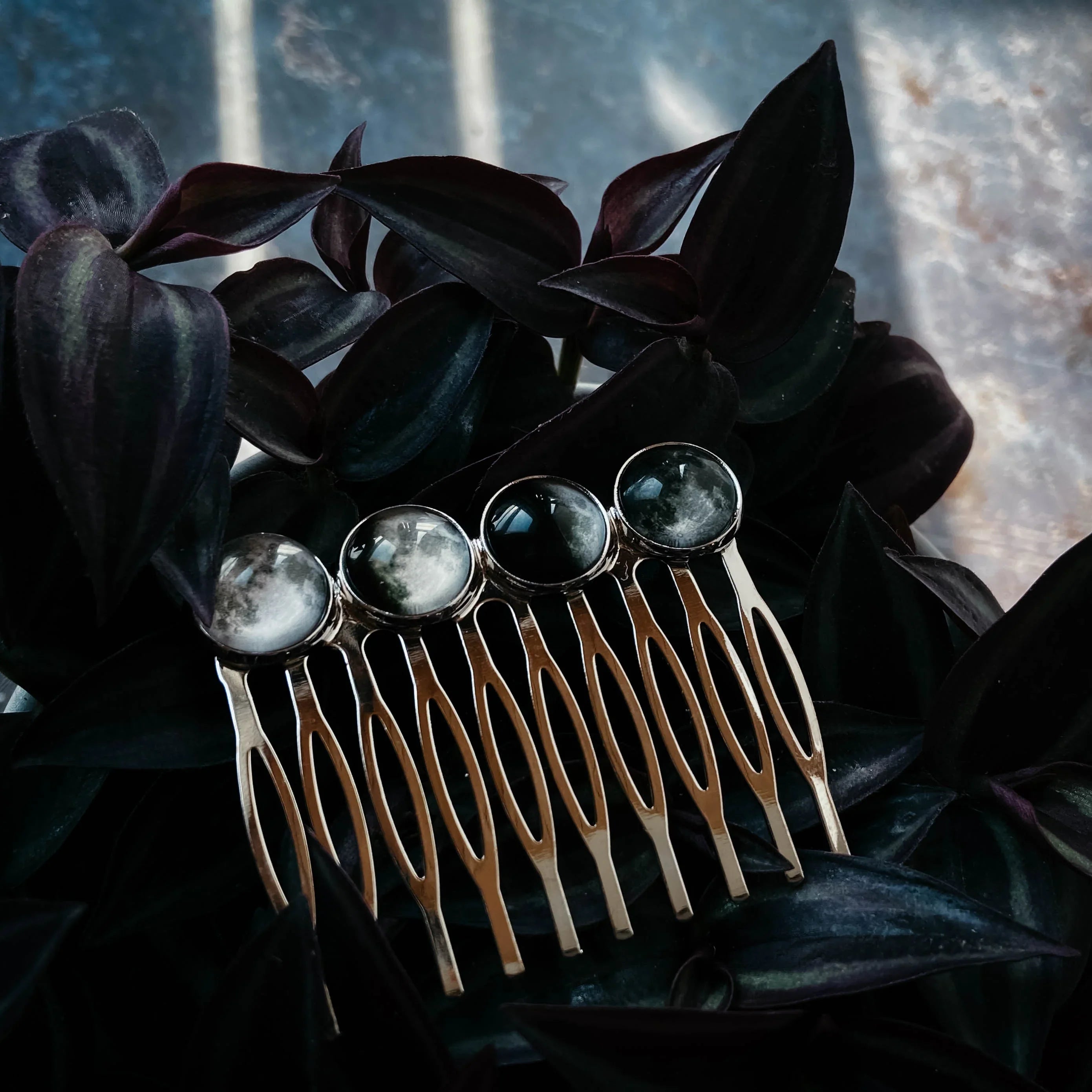 Gold hair comb with four round moonstone cabochons resting on dark purple leaves