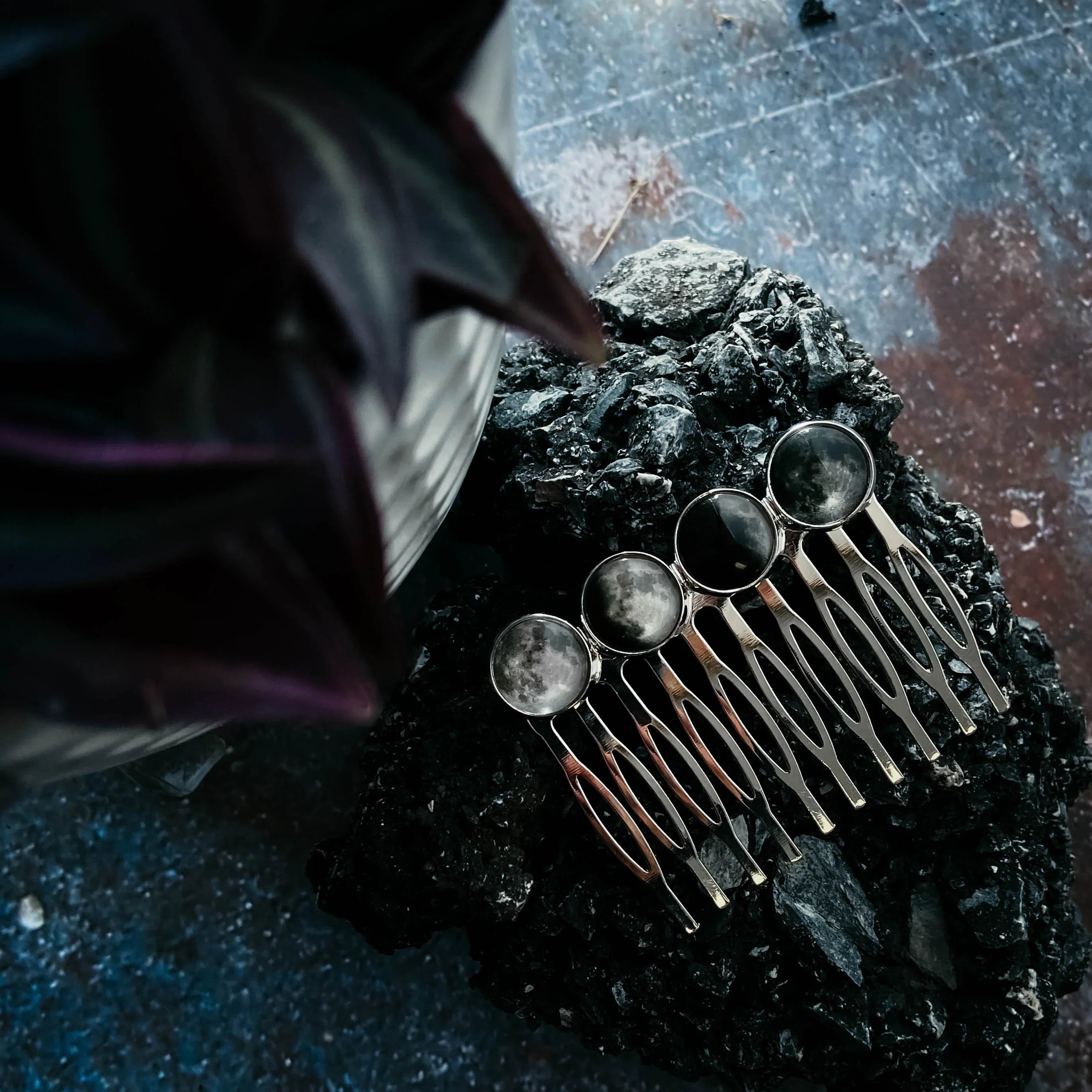 Set of five silver hairpins with moon phase designs placed on black textured rock