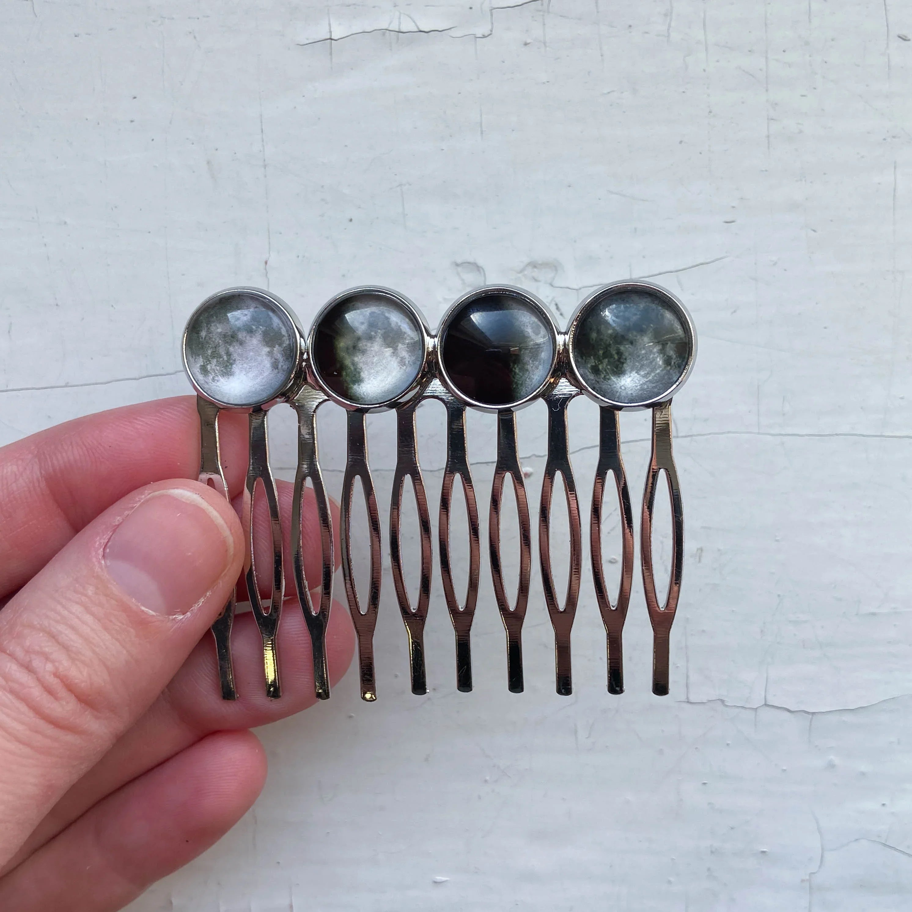 Hand holding silver metal hair comb with four round moon phase cabochon stones
