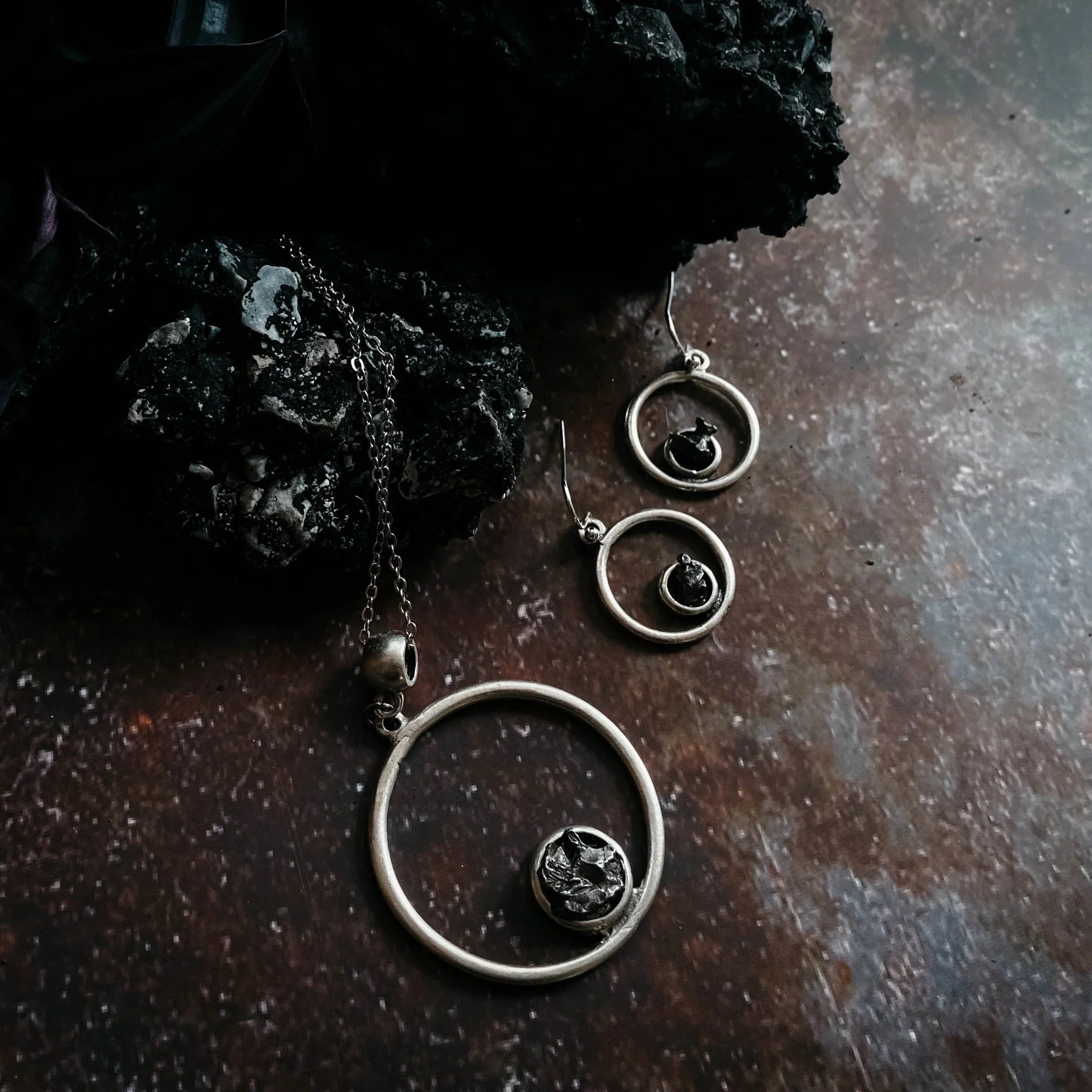 Silver circle pendant necklace and matching earrings with black textured stones on a dark rustic surface