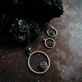 Silver circle pendant necklace and matching earrings with black textured stones on dark surface