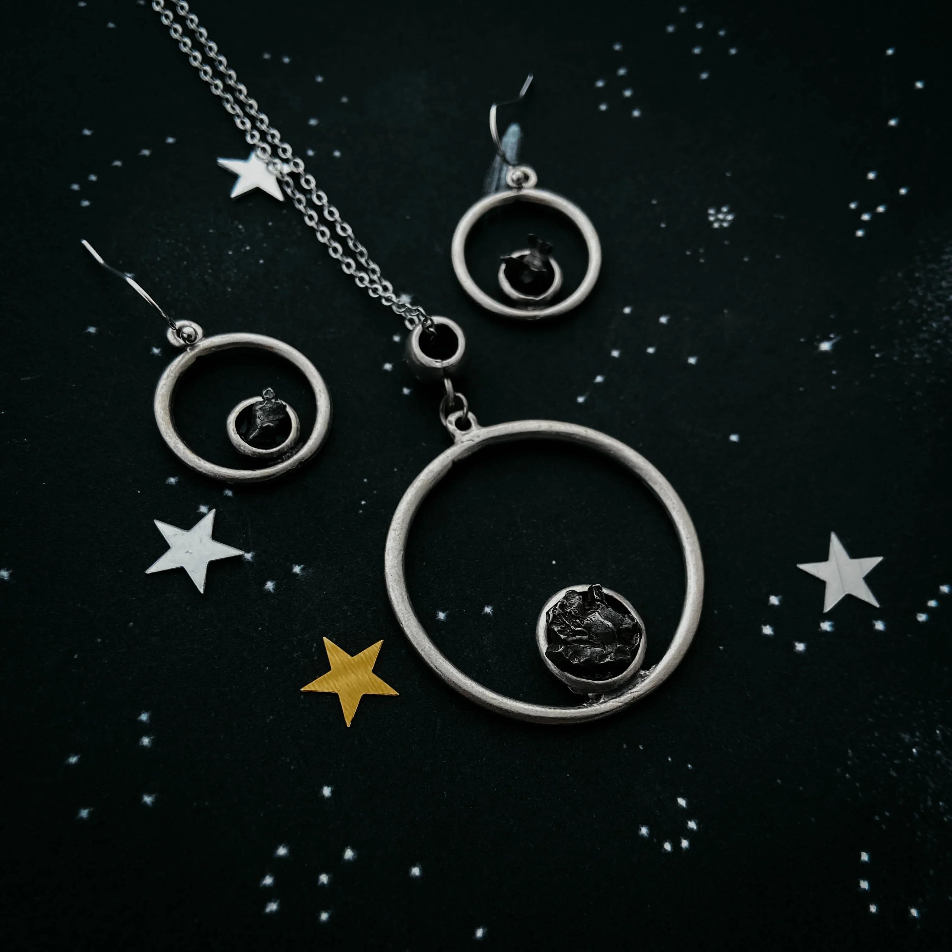 Silver hoop necklace and earrings set with black stone accents on starry dark background