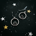 Silver hoop earrings with black stone center on starry night background with white and gold stars