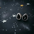 Silver earrings with black stones on starry, cosmic-themed background at Qu!rk Boutique
