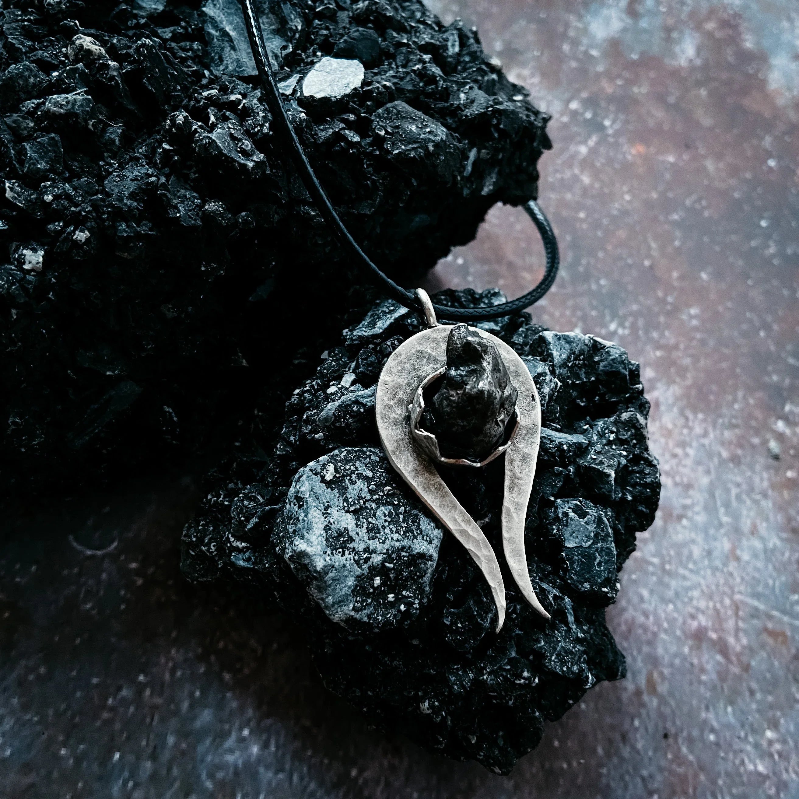 Silver pendant with a black raw stone on black textured volcanic rock background
