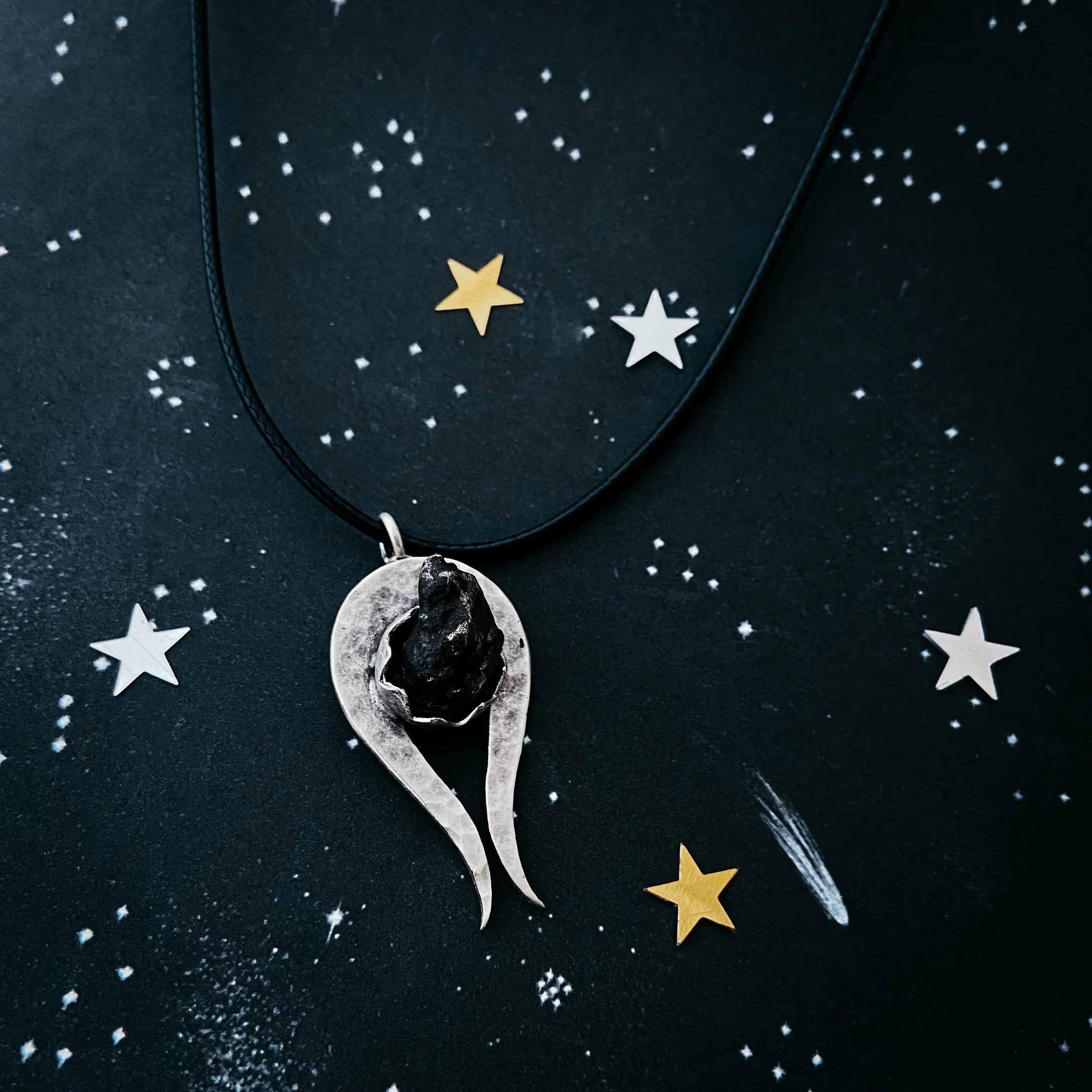 Silver pendant necklace with a black stone centerpiece on a starry space-themed background