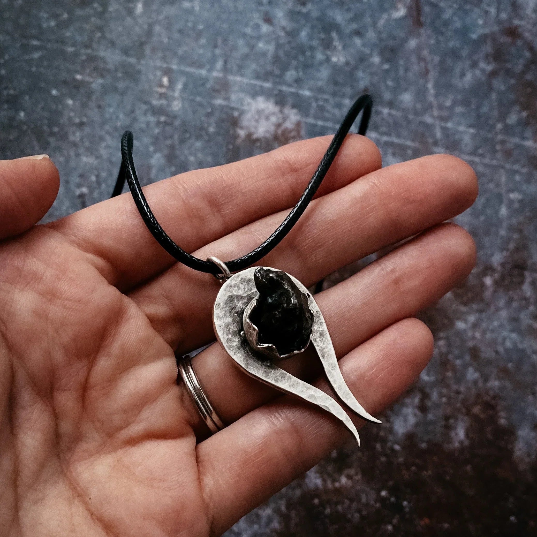 Hand holding a hammered silver pendant with a black textured stone on a black cord necklace