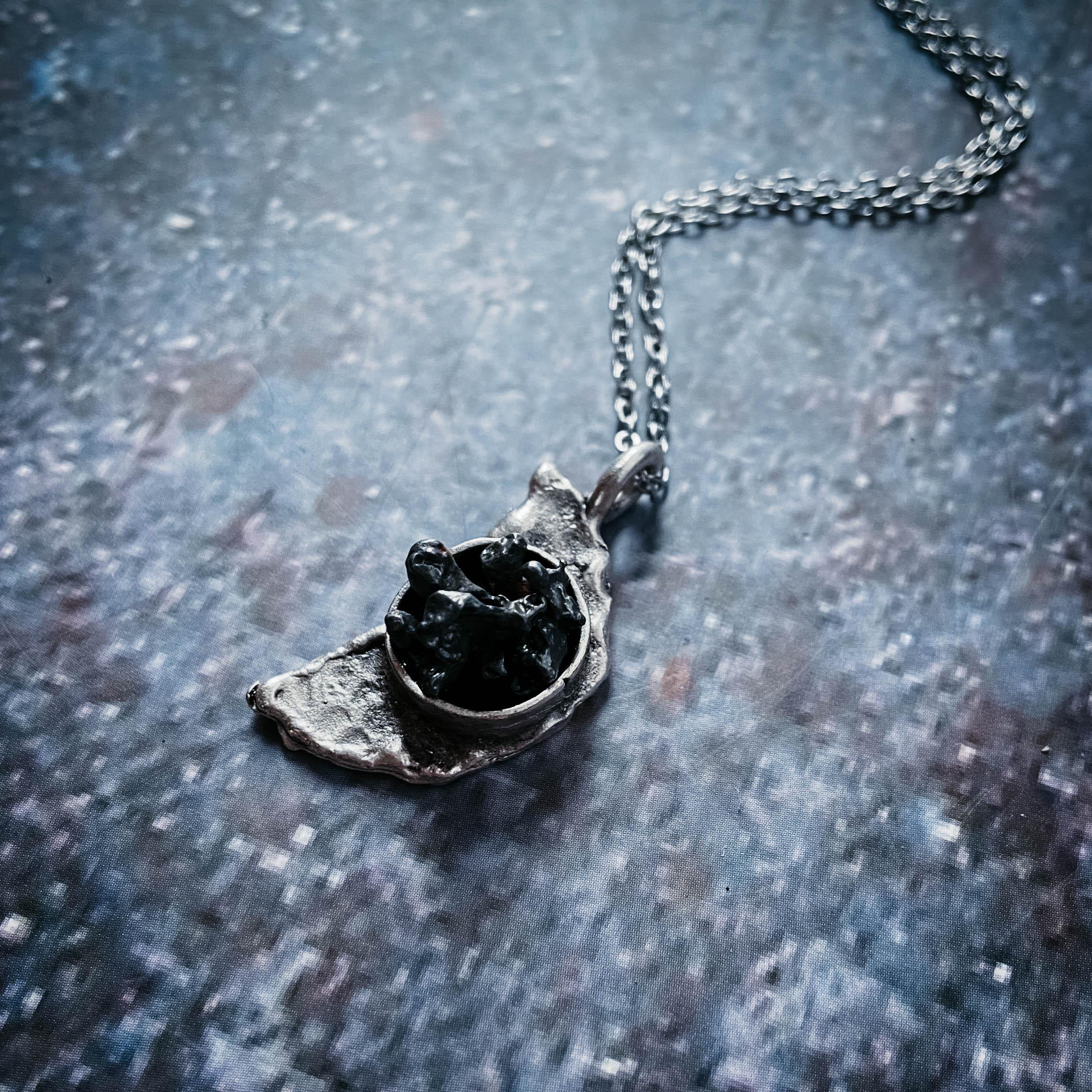 Unique silver pendant necklace with textured irregular shape and black rough stones on gray background