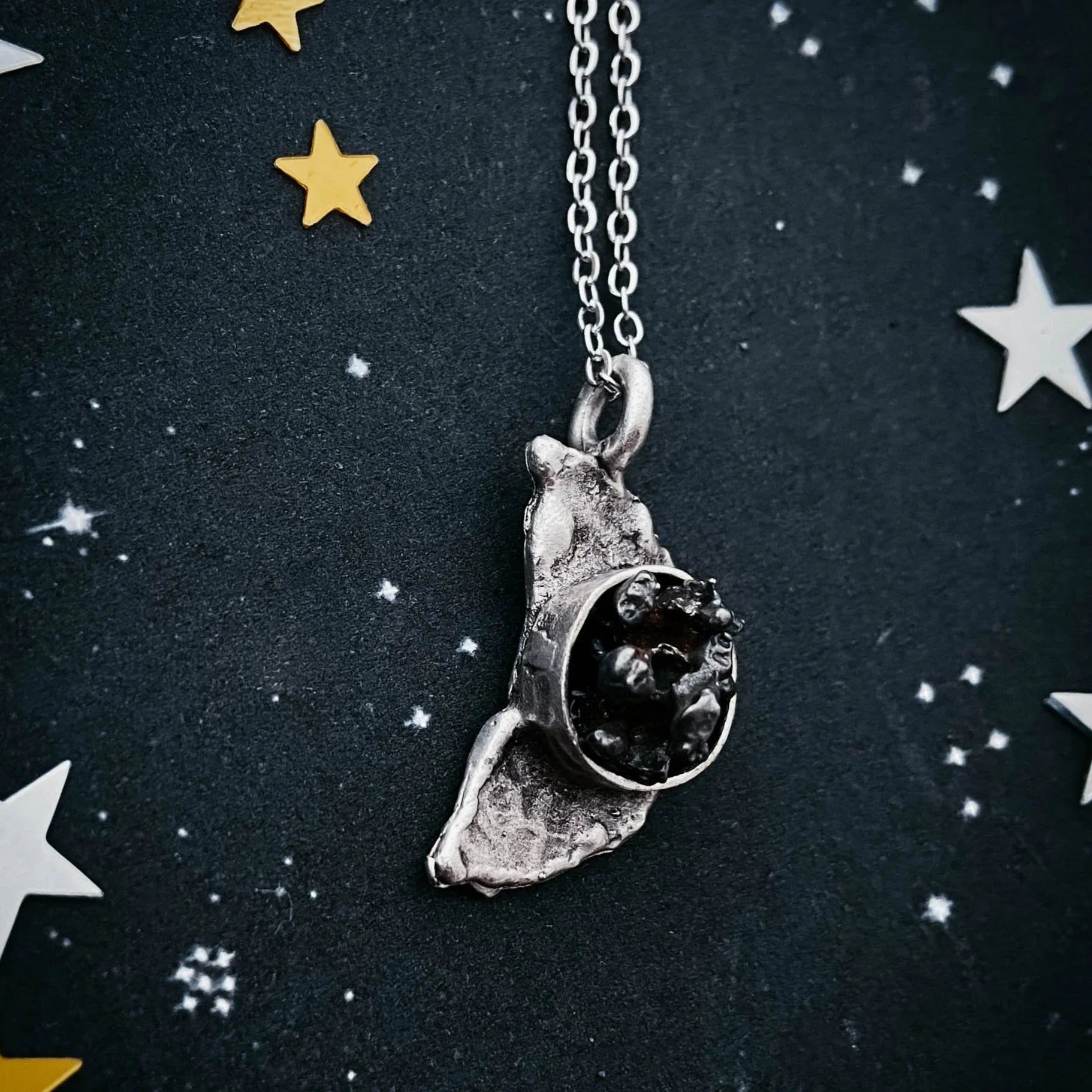 Silver pendant necklace with textured design and dark center stone on starry black background