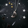 Silver textured pendant necklace on black starry background with silver and gold star confetti