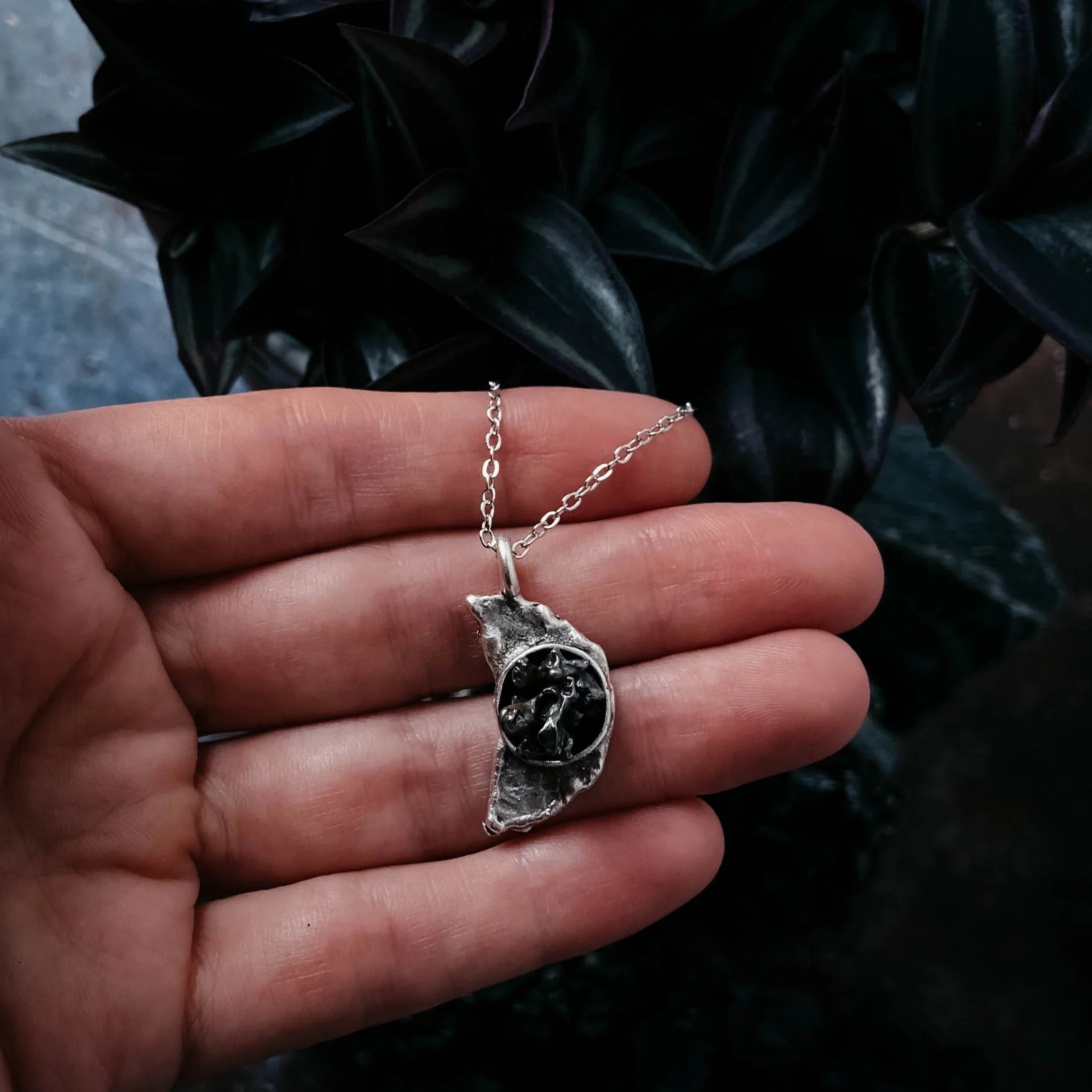 Hand holding unique silver pendant necklace with textured leaf design and black center detail