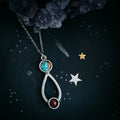 Silver pendant necklace with turquoise and red stones on black starry background with crystals