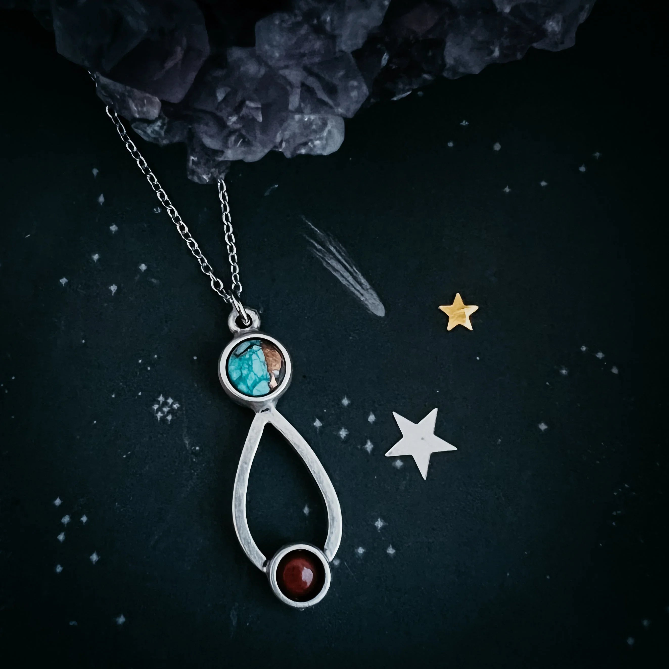 Silver pendant necklace with turquoise and red stones on black starry background with crystals