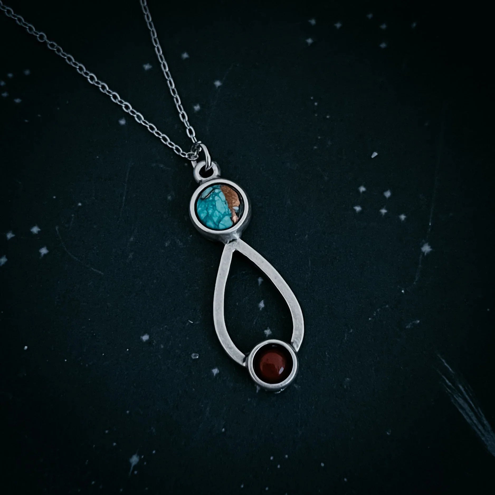 silver necklace with turquoise and red gemstone pendants on dark starry background