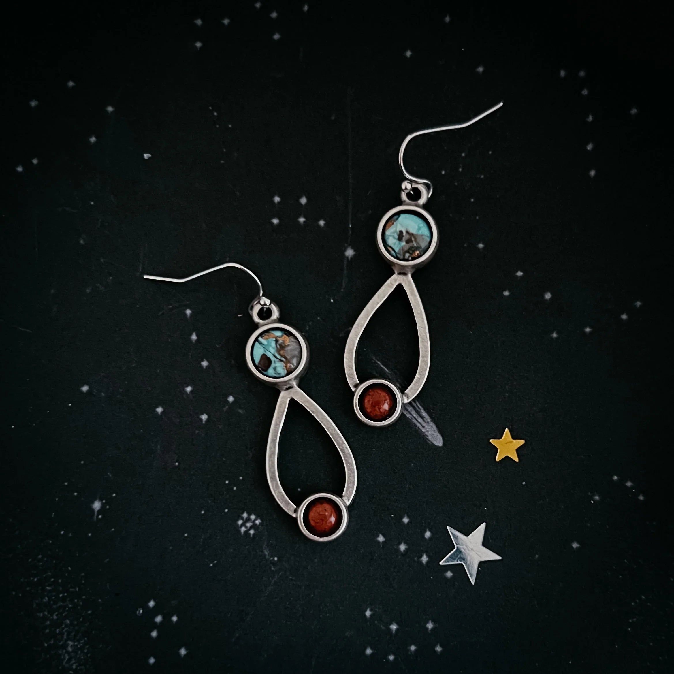 Artist-designed silver dangle earrings with turquoise and red stones on starry cosmic backdrop
