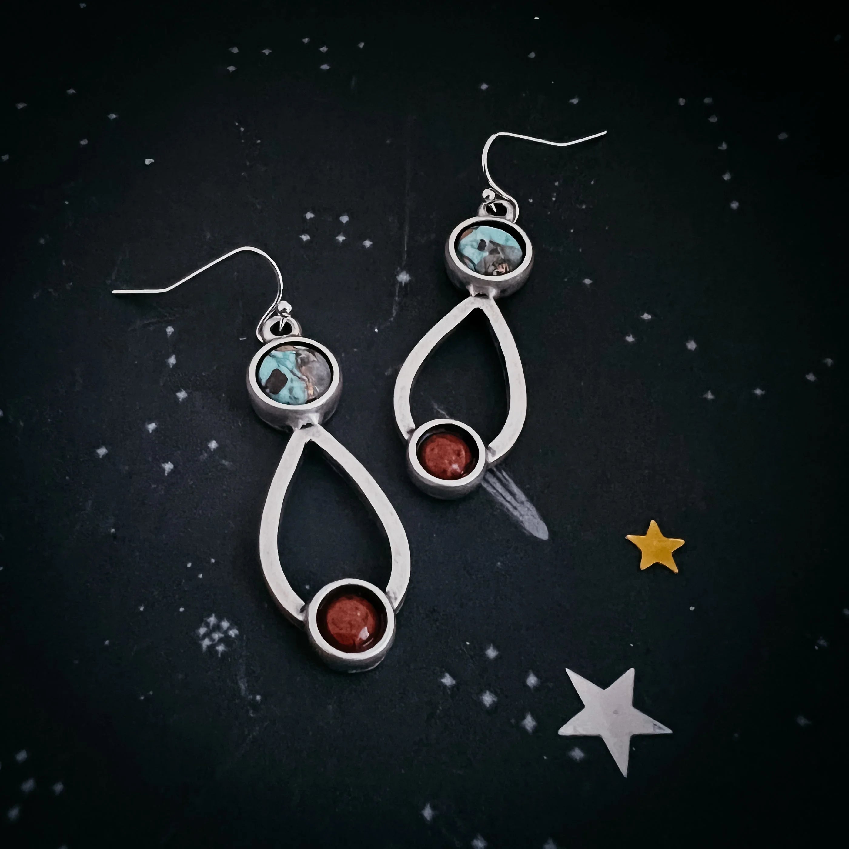Artist-designed silver drop earrings with turquoise and red stones on a cosmic star background