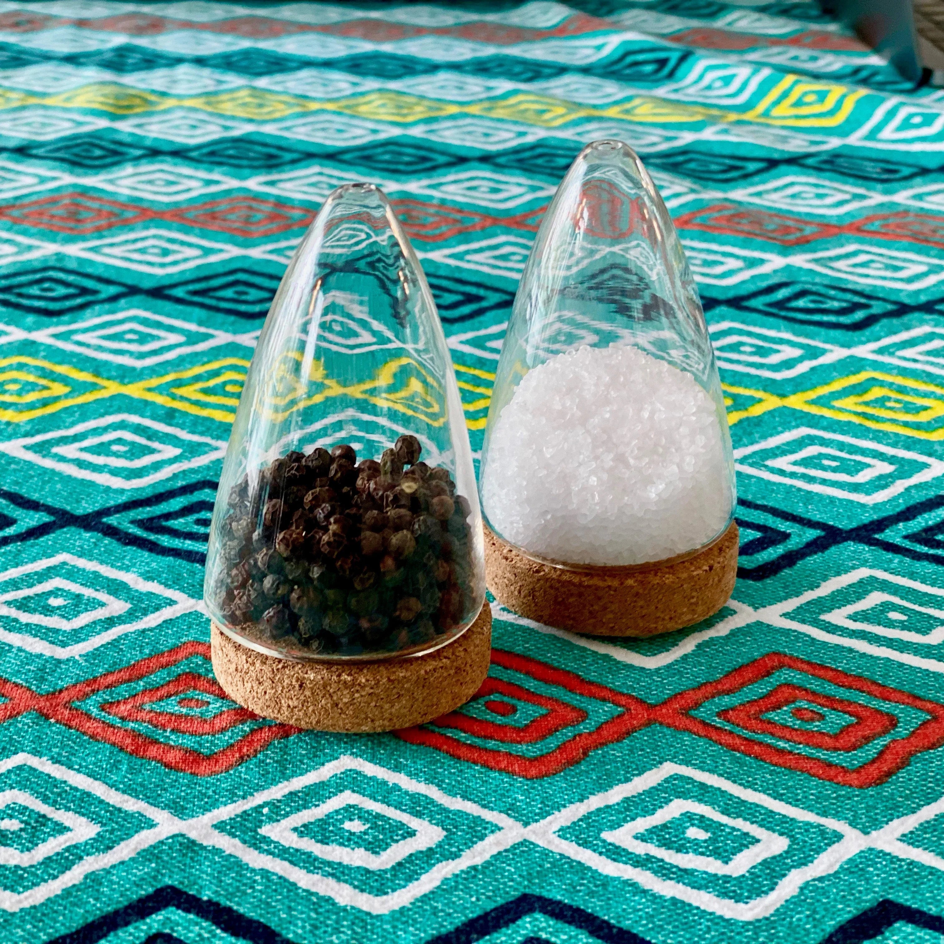 Modern salt and pepper shakers with glass domes and cork bases on a colorful geometric tablecloth